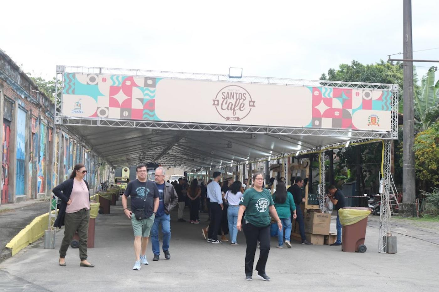 pessoas estaõ circulando sob tenda com fachada onde se lê Festival Santos Café 2024. #paratodosverem 