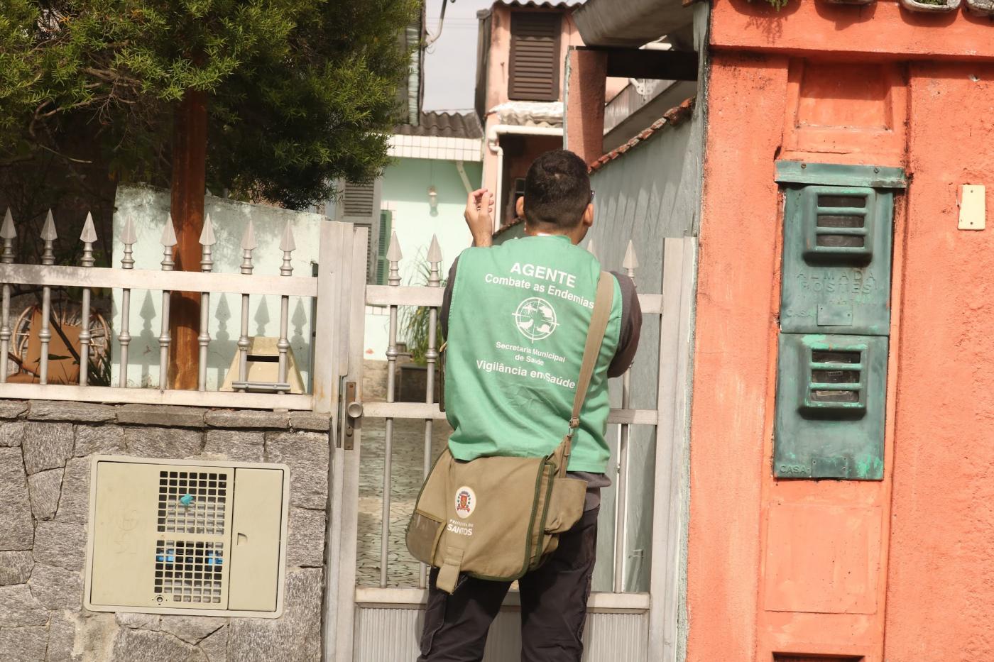 homem com colete de agente bate palma diante de casa. #paratodosverem