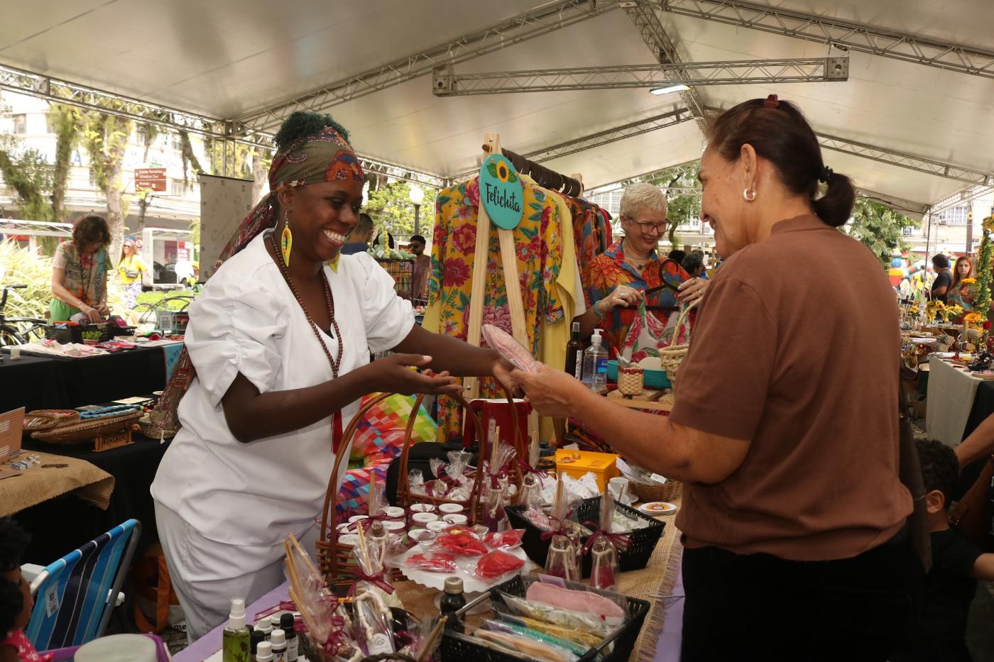 artesã apresenta produtos para consumidora em feira criativa. #paratodosverem