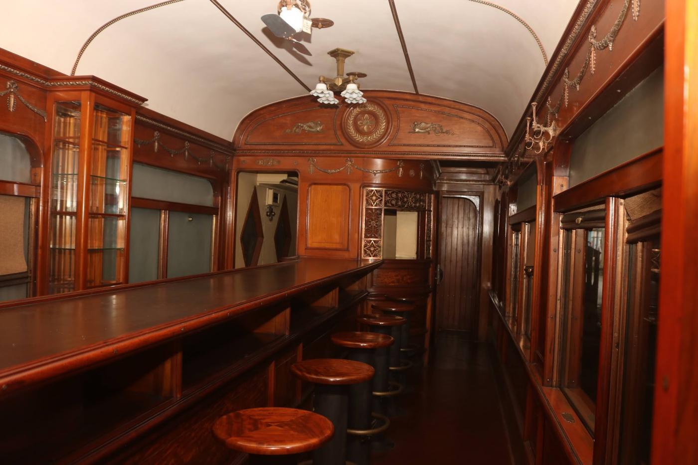 interior de carro ferroviário com balção de bar e bancos em madeira. #paratodosverem 