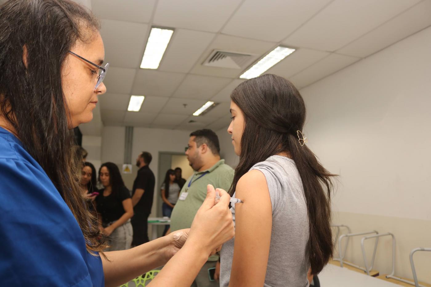 mulher vacina adolescente em sala de escola. #paratodosverem