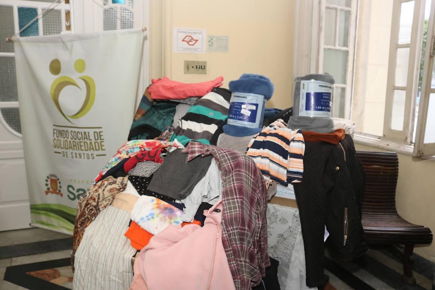 peças de roupas sobre uma mesa ao lado de banner do fundo social de solidariedade. #paratodosverem