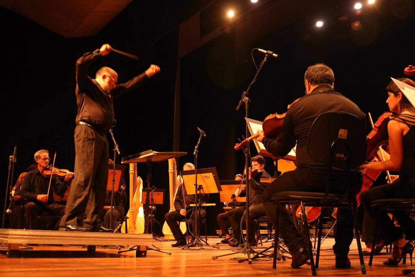 maestro em pé rege orquestra em palco. #paratodosverem