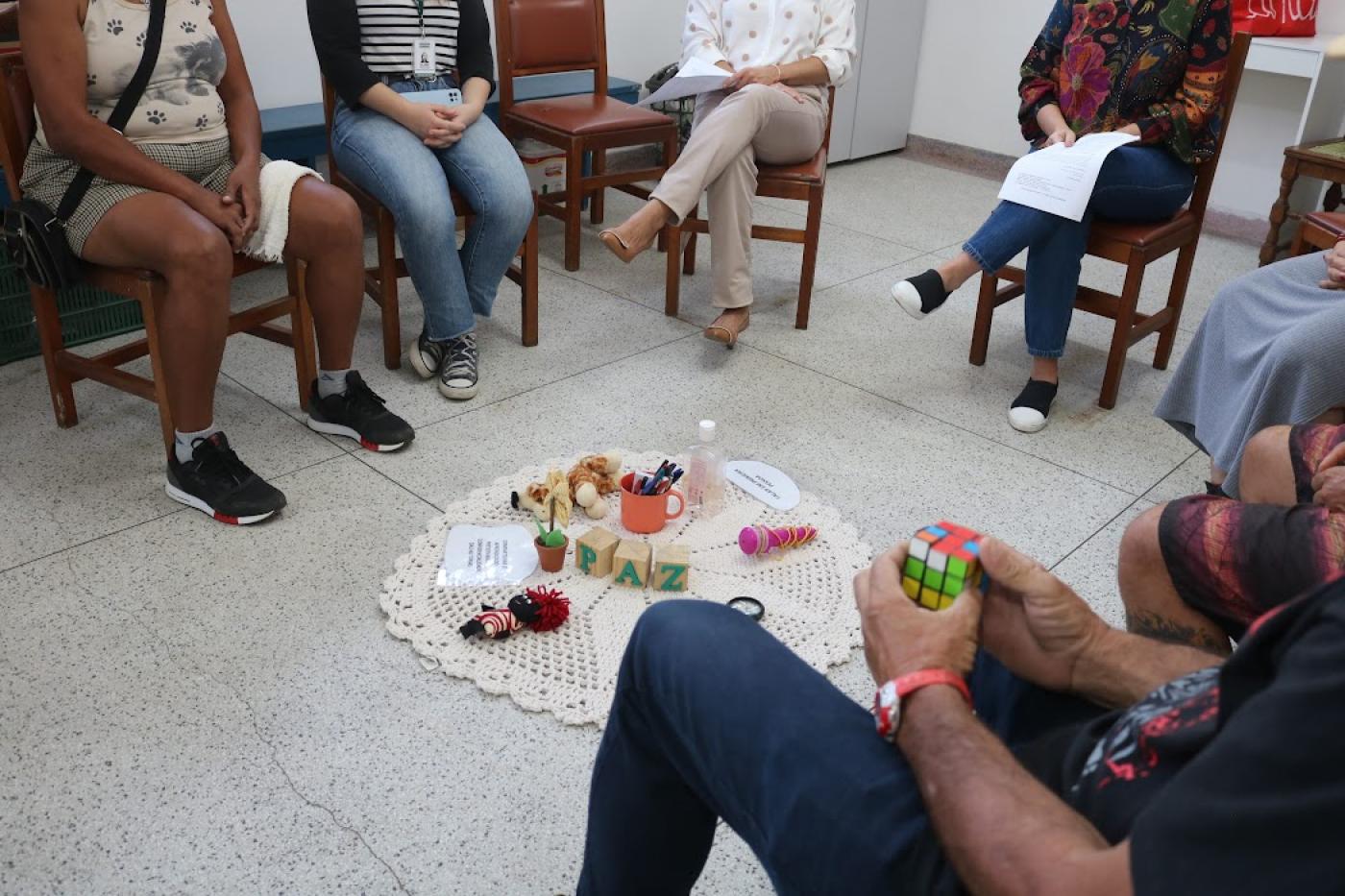 pessoas sentadas em circulo com objetos no centro no tapete #paratodosverem