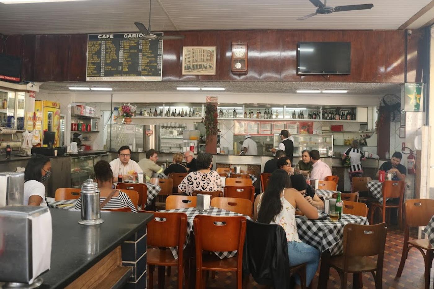 Bar com várias pessoas sentadas na mesa. #paratodosverem