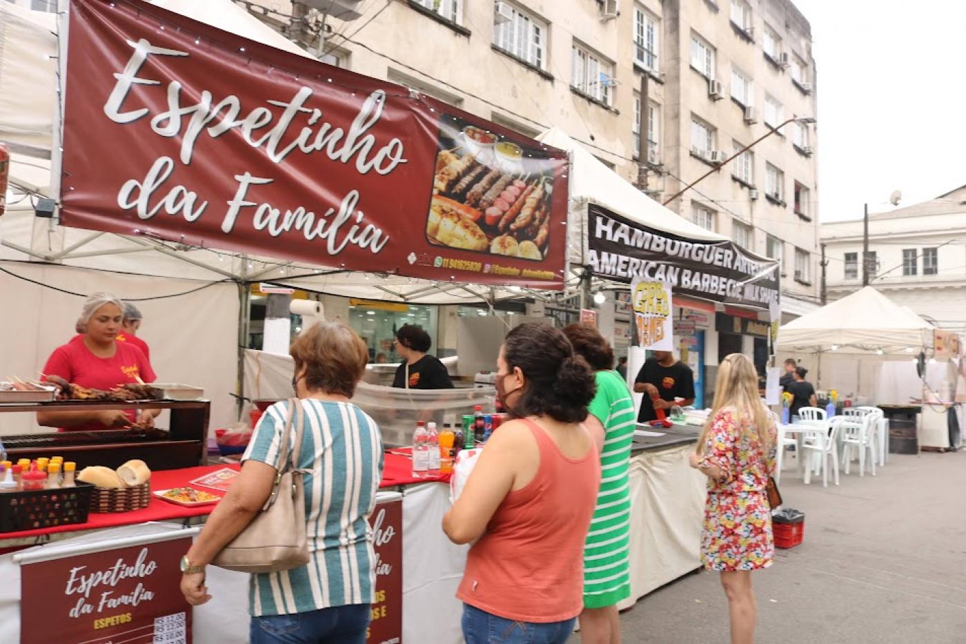 Barracas de comida em praça com pessoas circulando. #paratodosverem