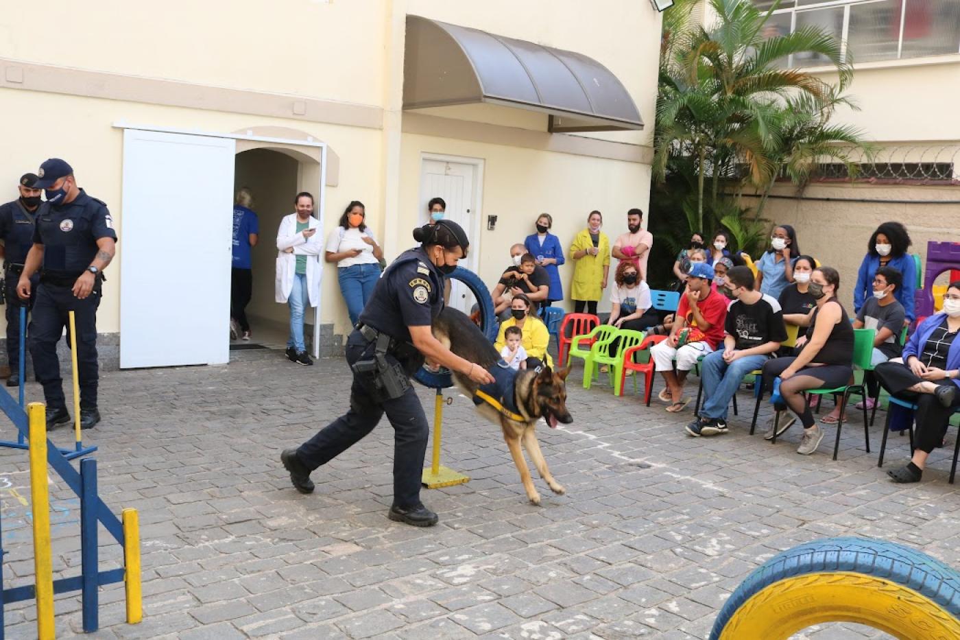 guarda conduz cachorro que pula enquanto pessoas observam #paratodosverem