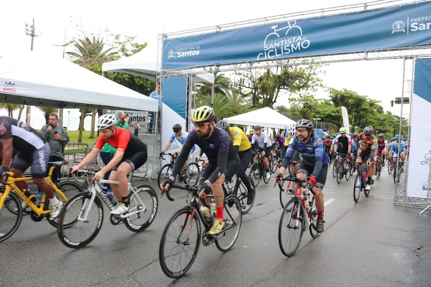 Largada da prova com ciclistas abaixo do portal. Prova é na orla. #paratodosverem