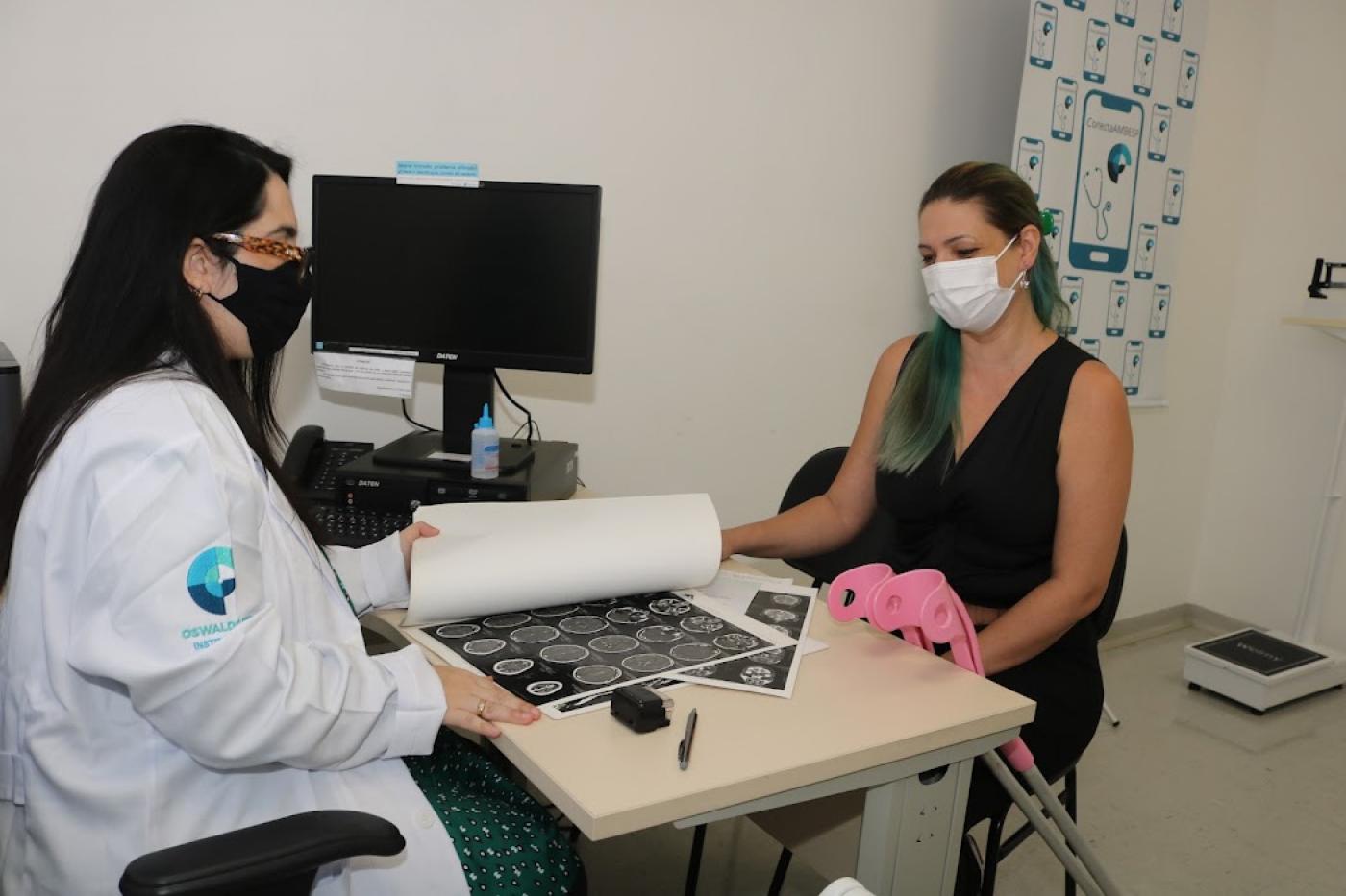 medica está com exame aberto na mesa e atendendo uma mulher. #paratodosverem