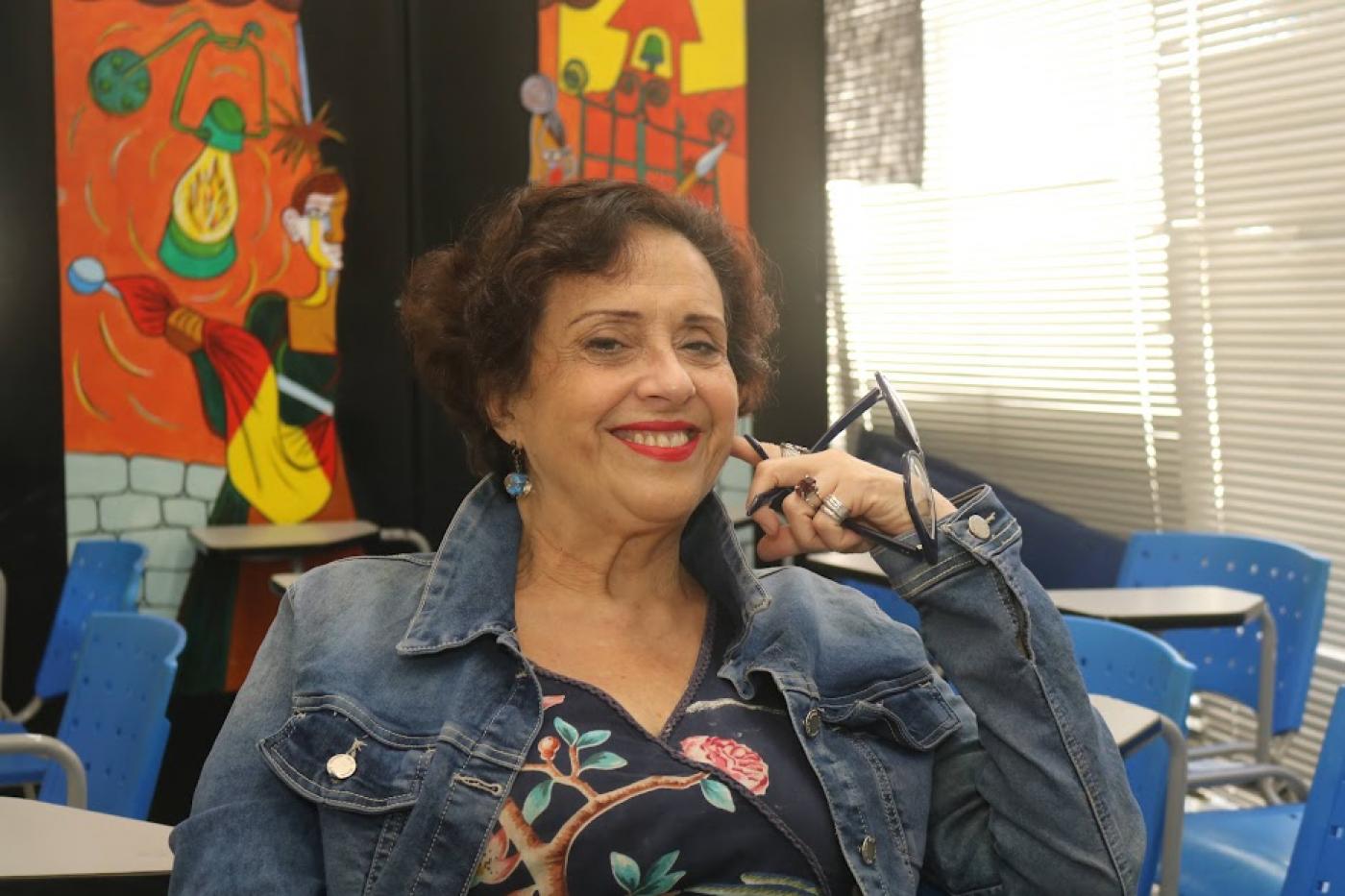 mulher sorri para foto segurando óculos na mão esquerda e encostada ao rosto. #paratodosverem 