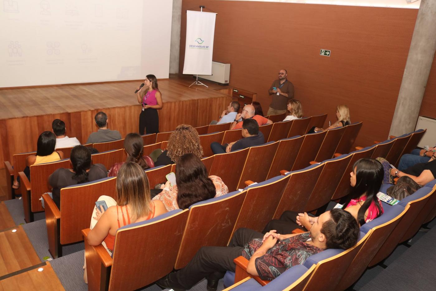 pessoas assistem palestra sentadas em auditório. #paratodosverem