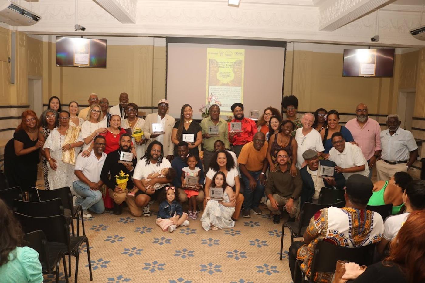 várias pessoas reunidas posam para foto. Algumas seguram placas. #paratodosverem 