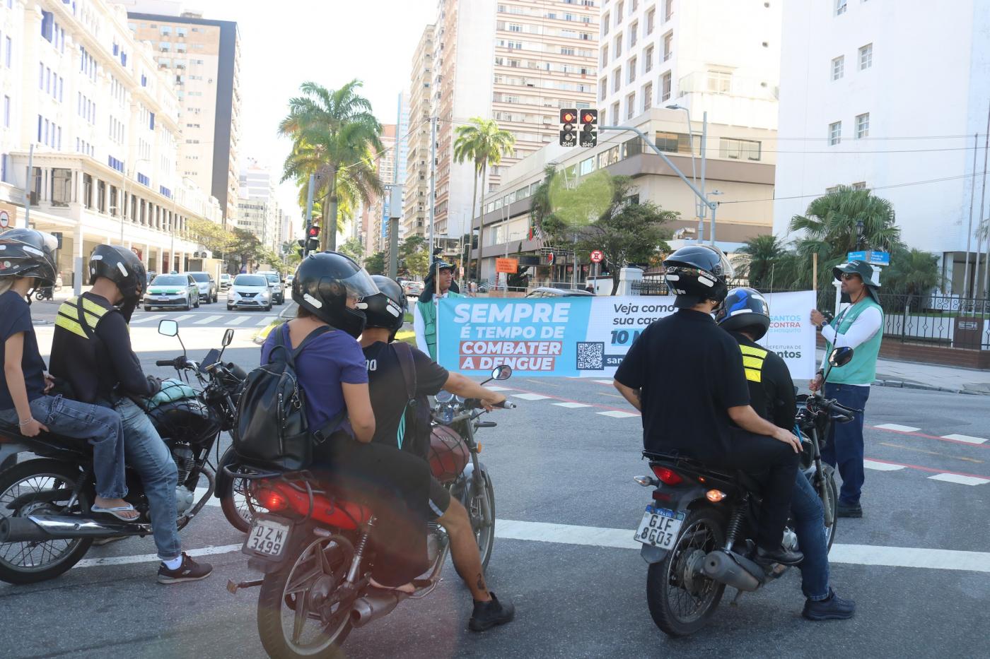 motociclistas parados diante de faixa sobre dengue. #paratodosverem