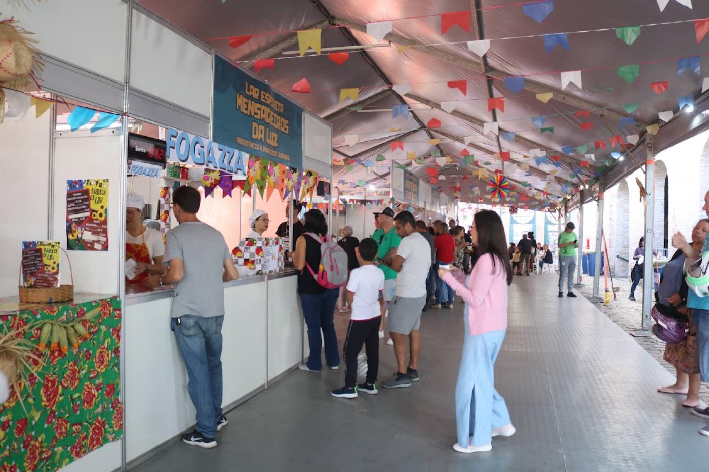 pessoas se aproximando de barracas da festa inverno #paratodosverem
