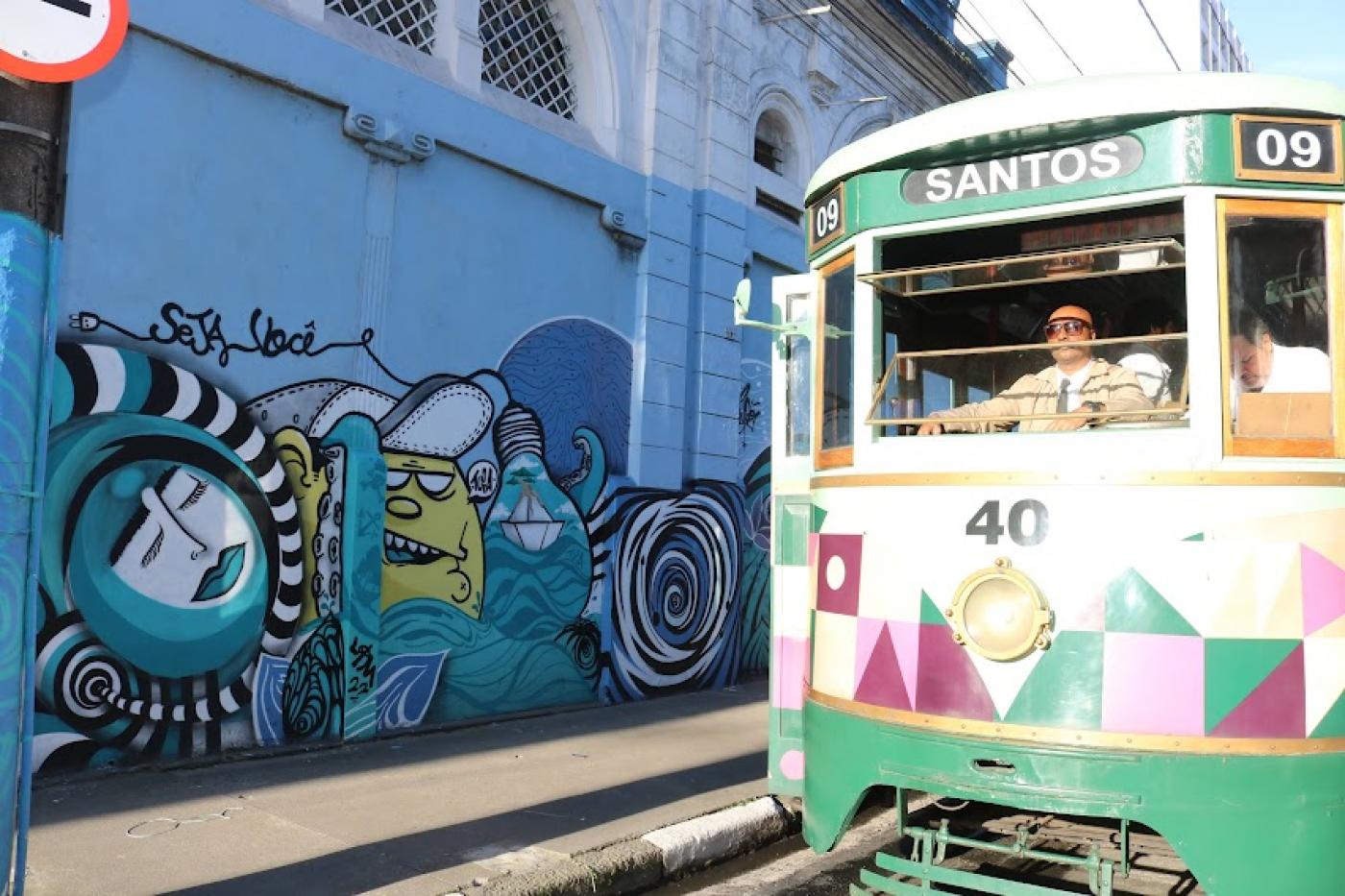 grafite em muro com bonde passando ao lado. #paratodosverem