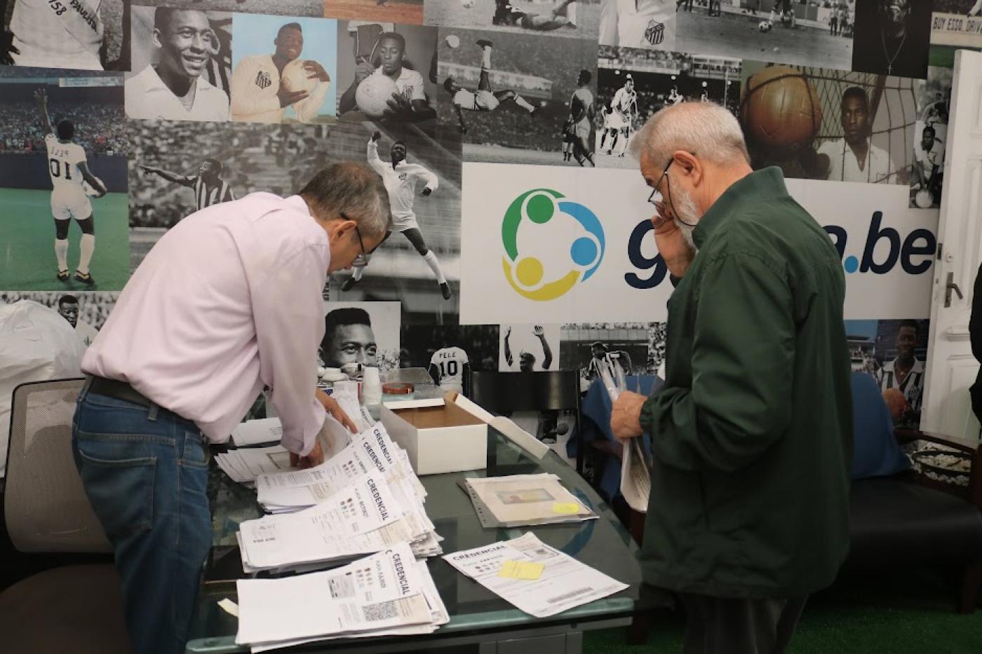 homem está mexendo em pilhas de papeis onde se lê no alto: credencial. #paratodosverem