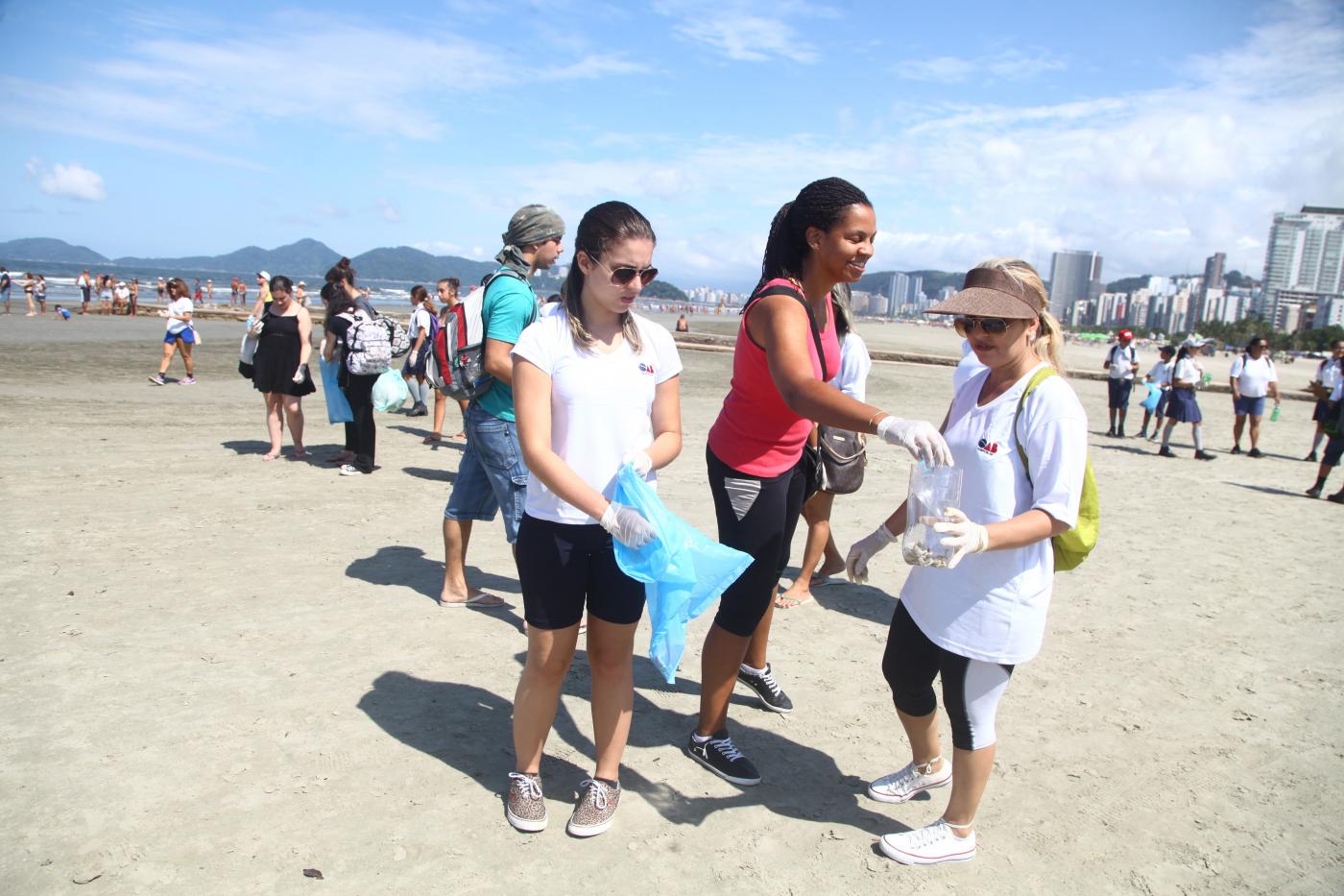 Mulheres recolhem lixo com sacolas na praia #pracegover 