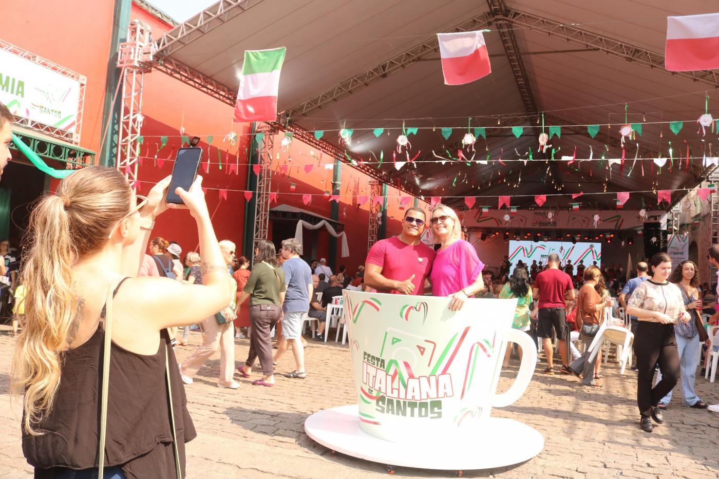 mulher fotografa casal dentro de xícara instagramável do evento. #paratodosverem
