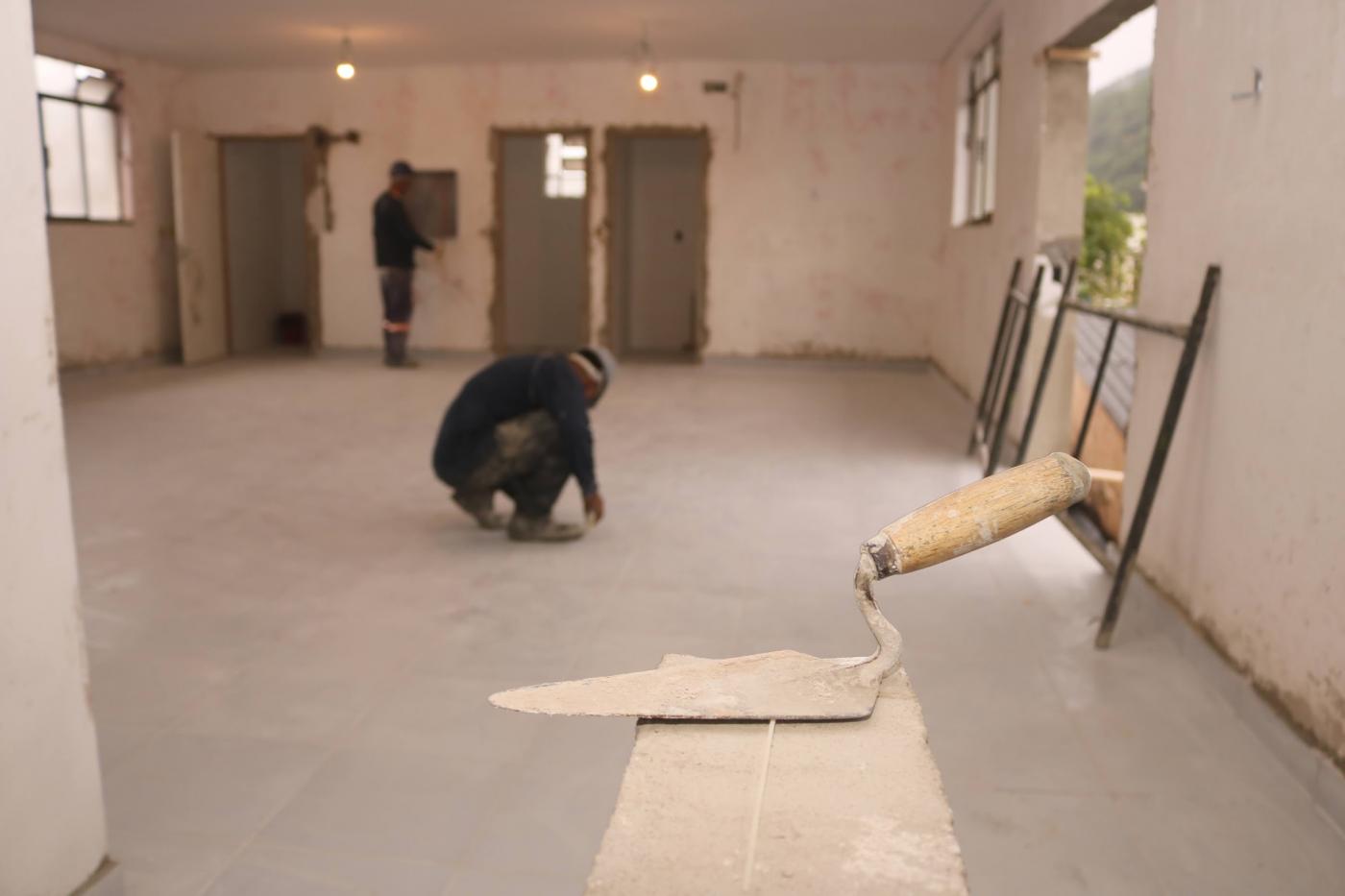 pá de pedreiro em primeiro plano e homens ao fundo. #paratodosverem