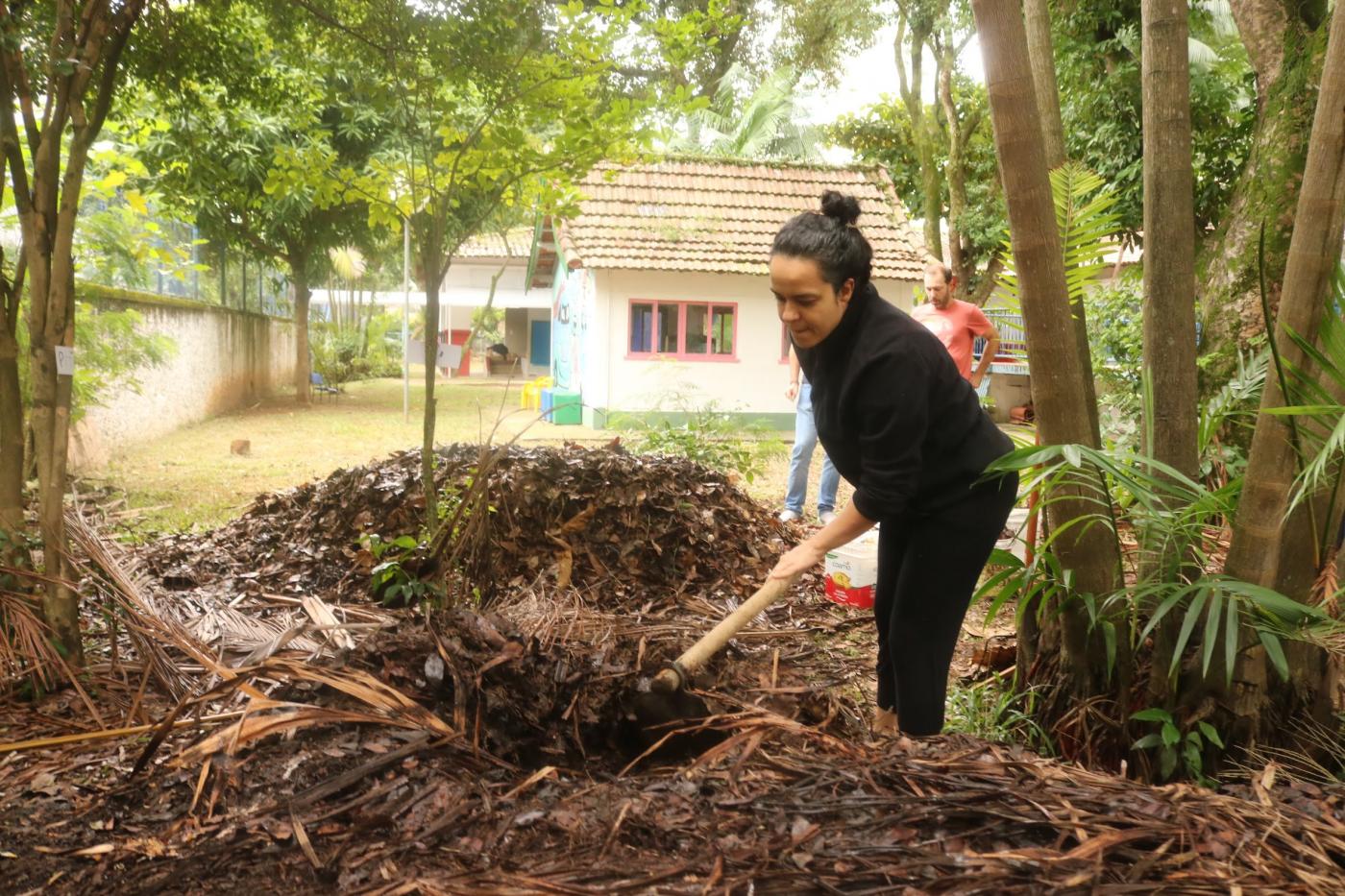 mulher está revolvendo material orgânico em jardim. #paratodosverem