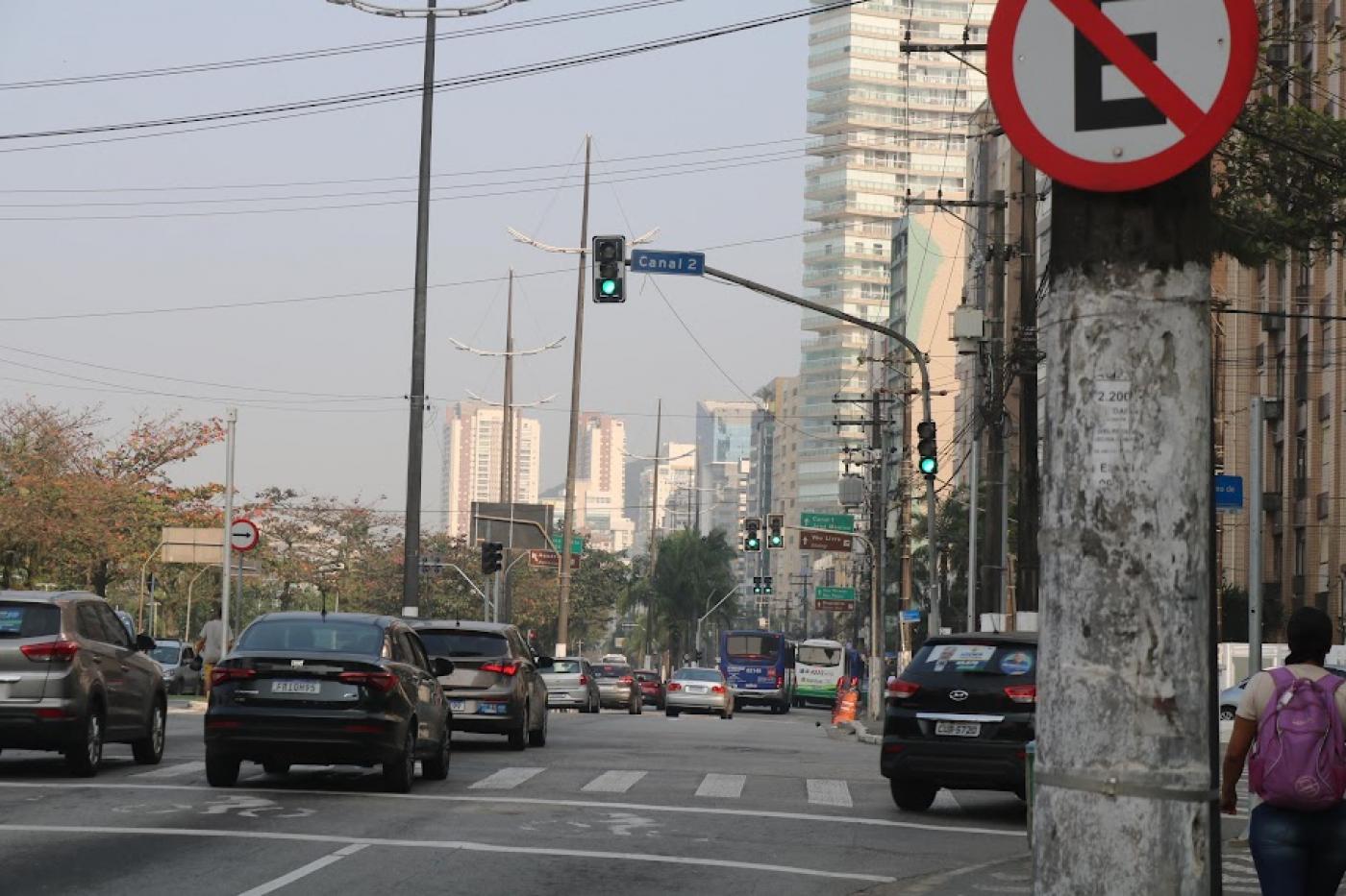 avenida com veículos circulando e semáforos todos em verde, abertos ao fluxo. #paratodosverem 