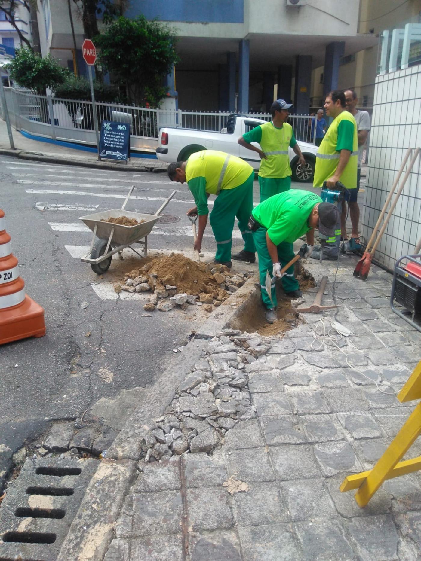 quatro homens estão trabalhando em esquina de rua, rebaixando a rua. #paratodosverem