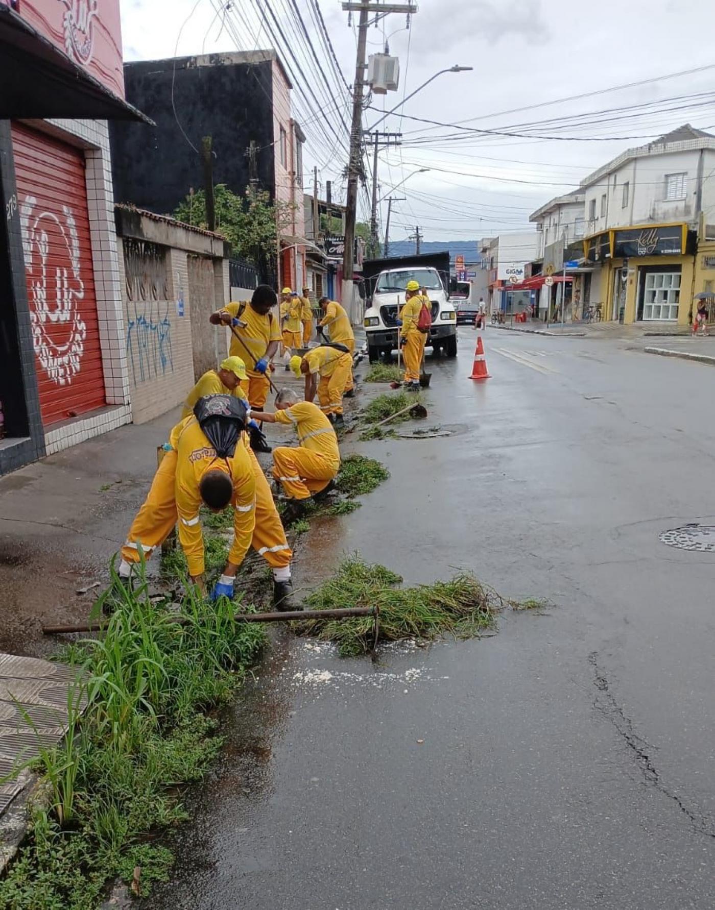 grupo de homens uniformizados está retirando mato junto à guia em rua. #paratodosverem 