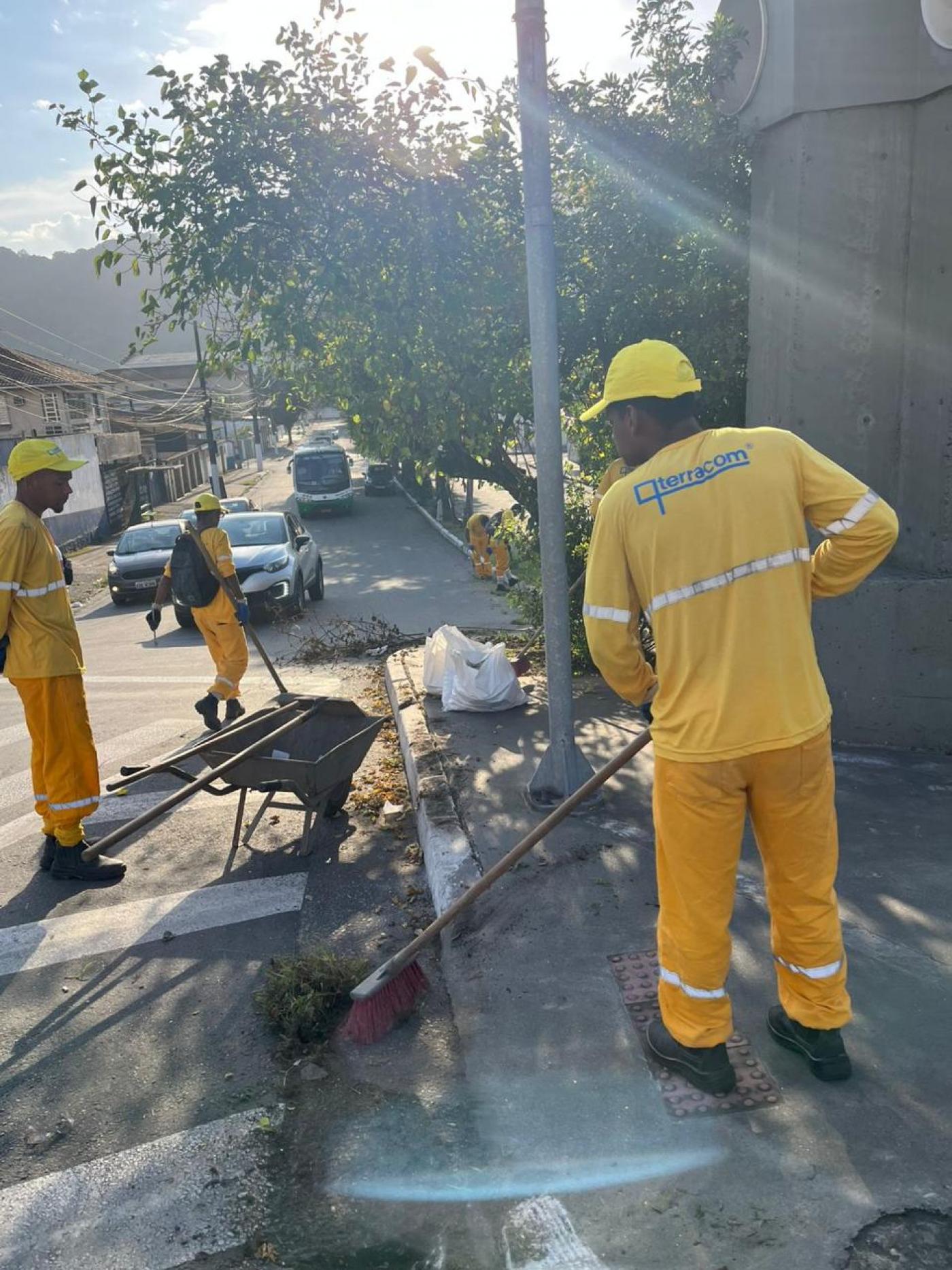 homens uniformizados estão varrendo material capinado de calçada e guia. #paratodosverem 