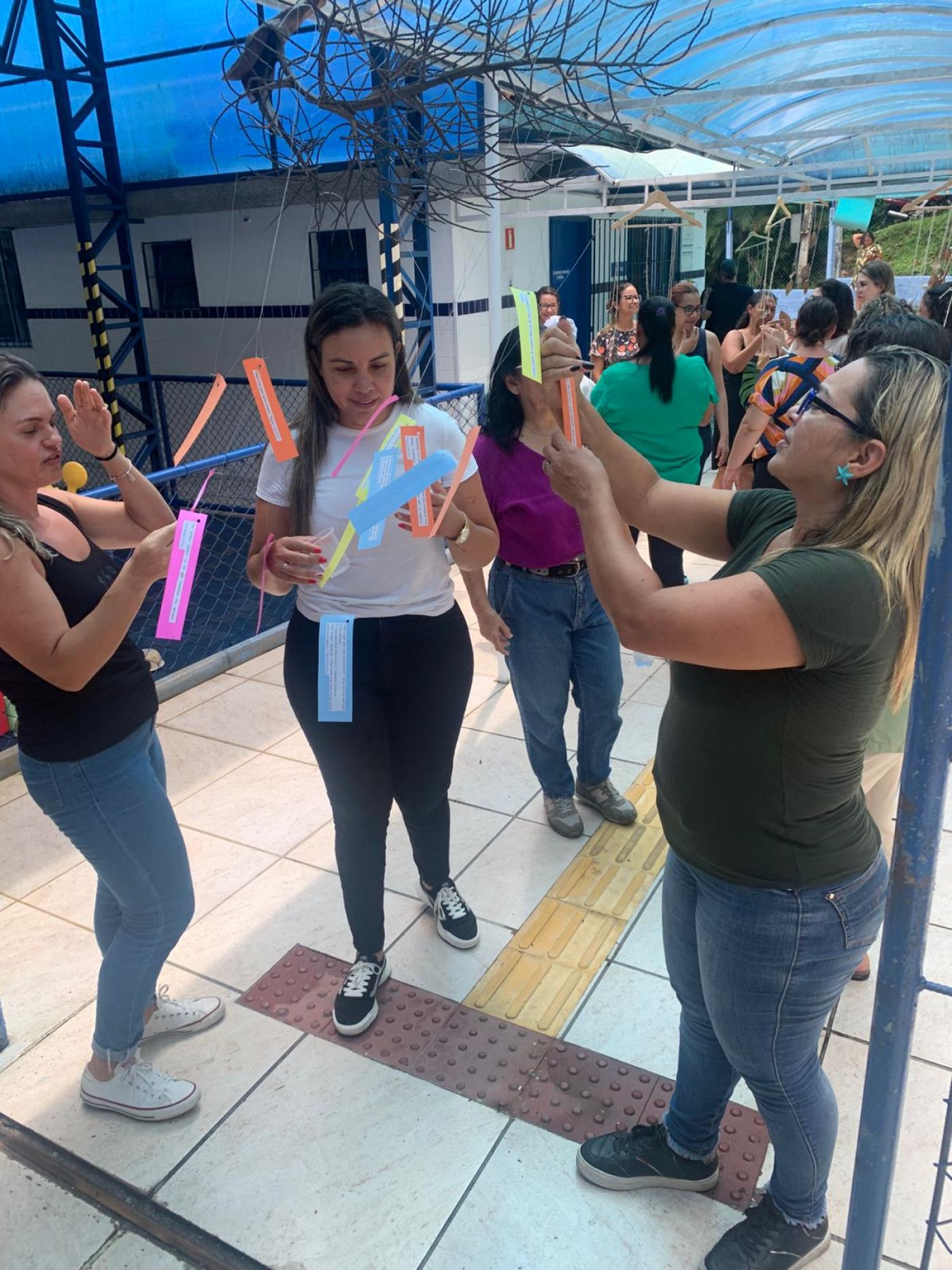 professores estão em pé em corredor lendo mensagens e fotos penduradas em fios. #paratodosverem 