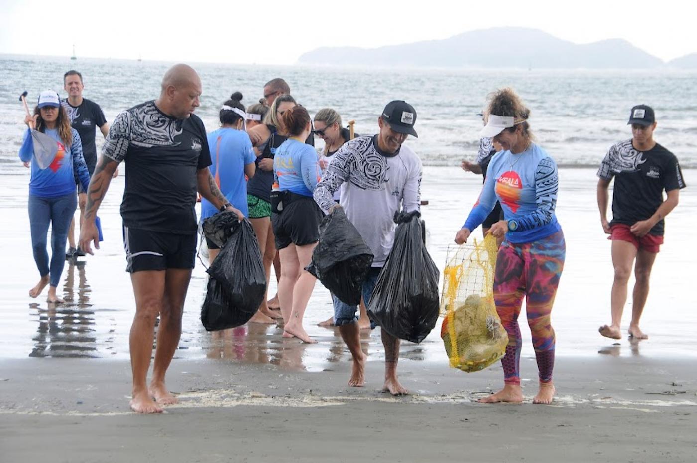 Praticantes estão na beira do mar com sacos onde estão depositados resíduos. 