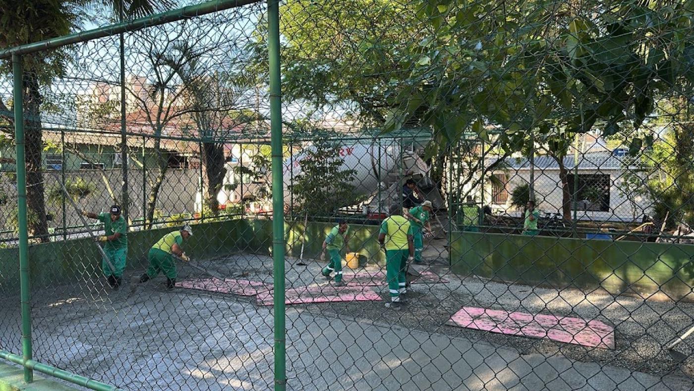 quadra com alambrado e homens trabalhando no interior. #paratodosverem
