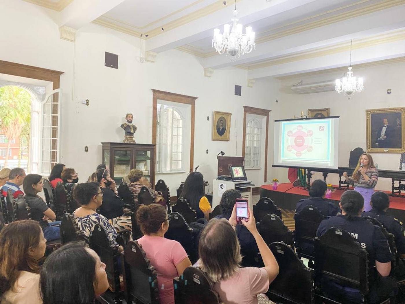 servidoras sentadas em auditório assistindo palestra. #paratodosverem