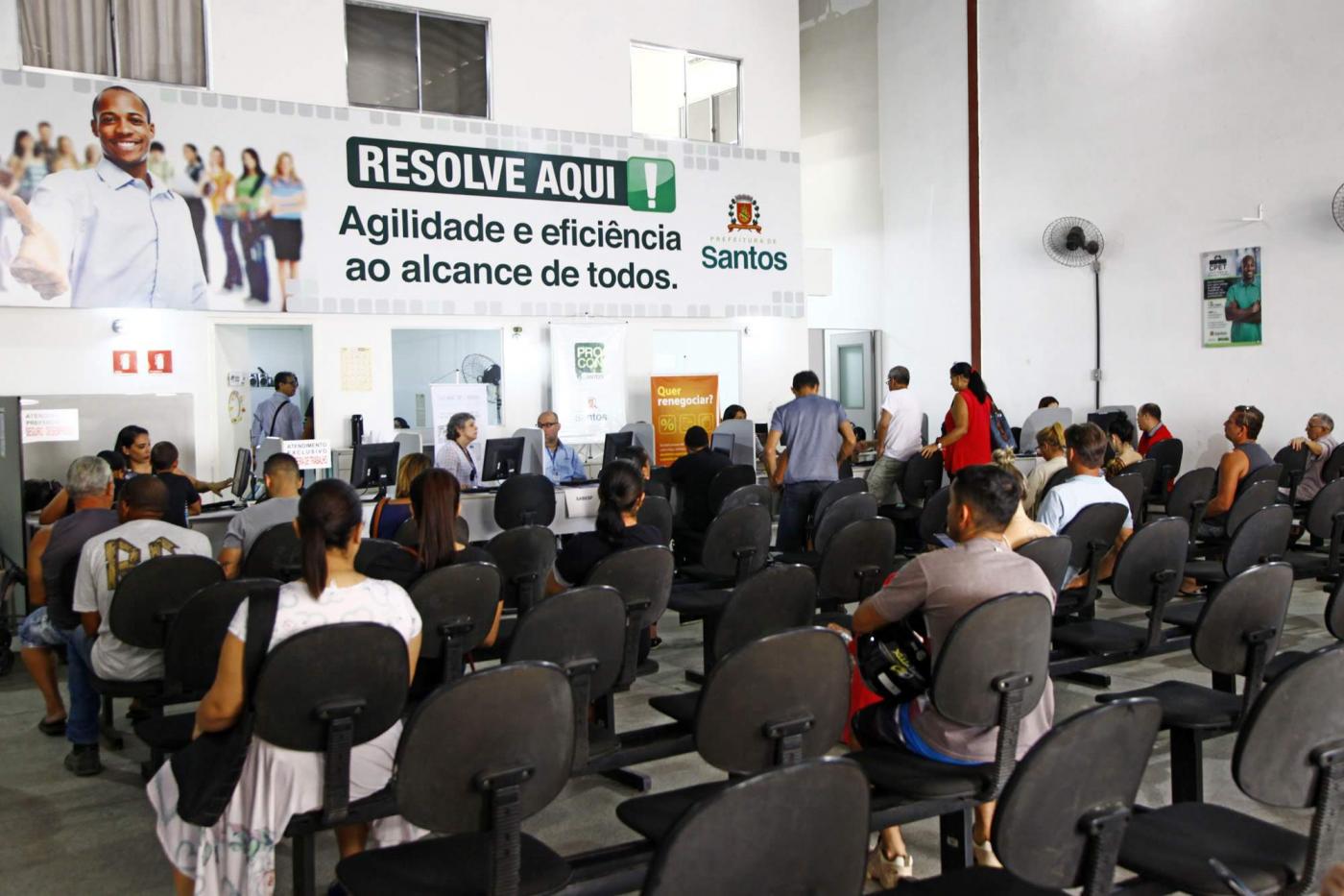 O salão do Resolve Aqui com diversas pessoas sentadas nos bancos aguardando atendimento. #Pracegover