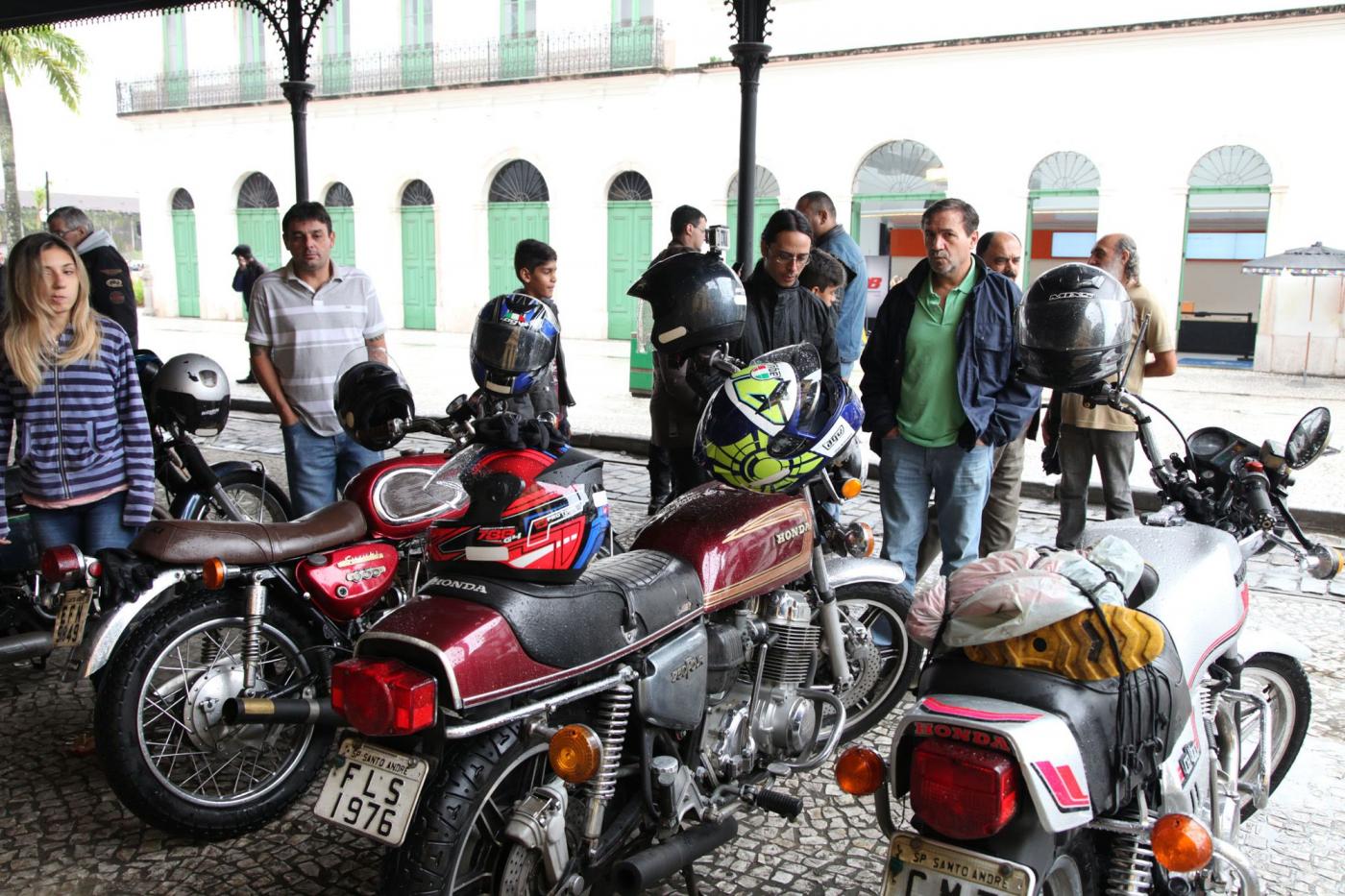 Motos raras em exposição na rua sob marquise. Público as observa