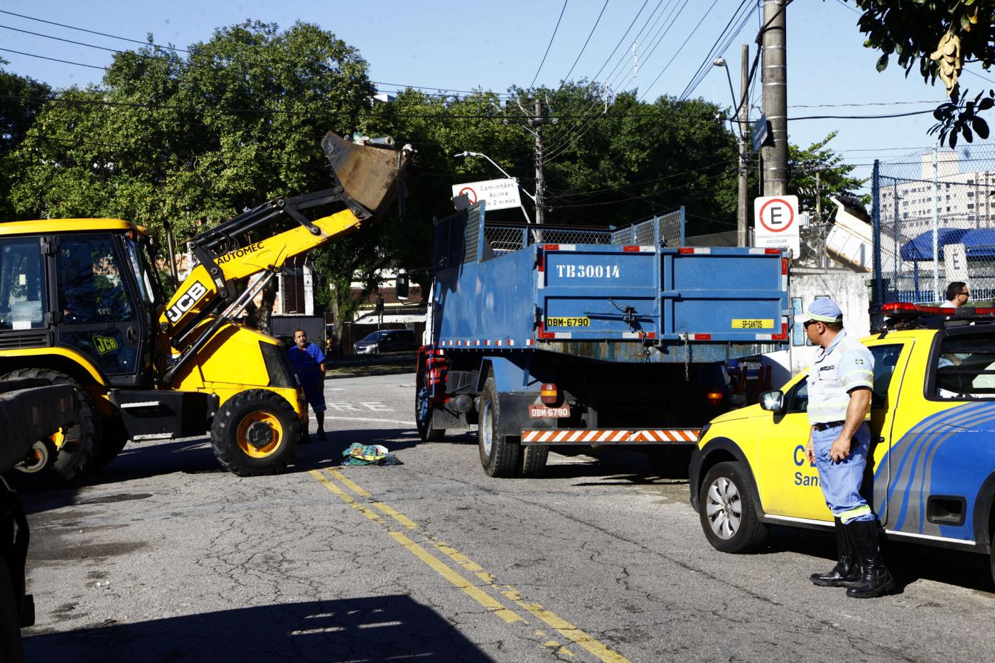 Máquina retroescavadeira transfere materiais recolhidos para caminhão. Acompanhando o trabalho está o carro e um agente da CET. #Pracegover