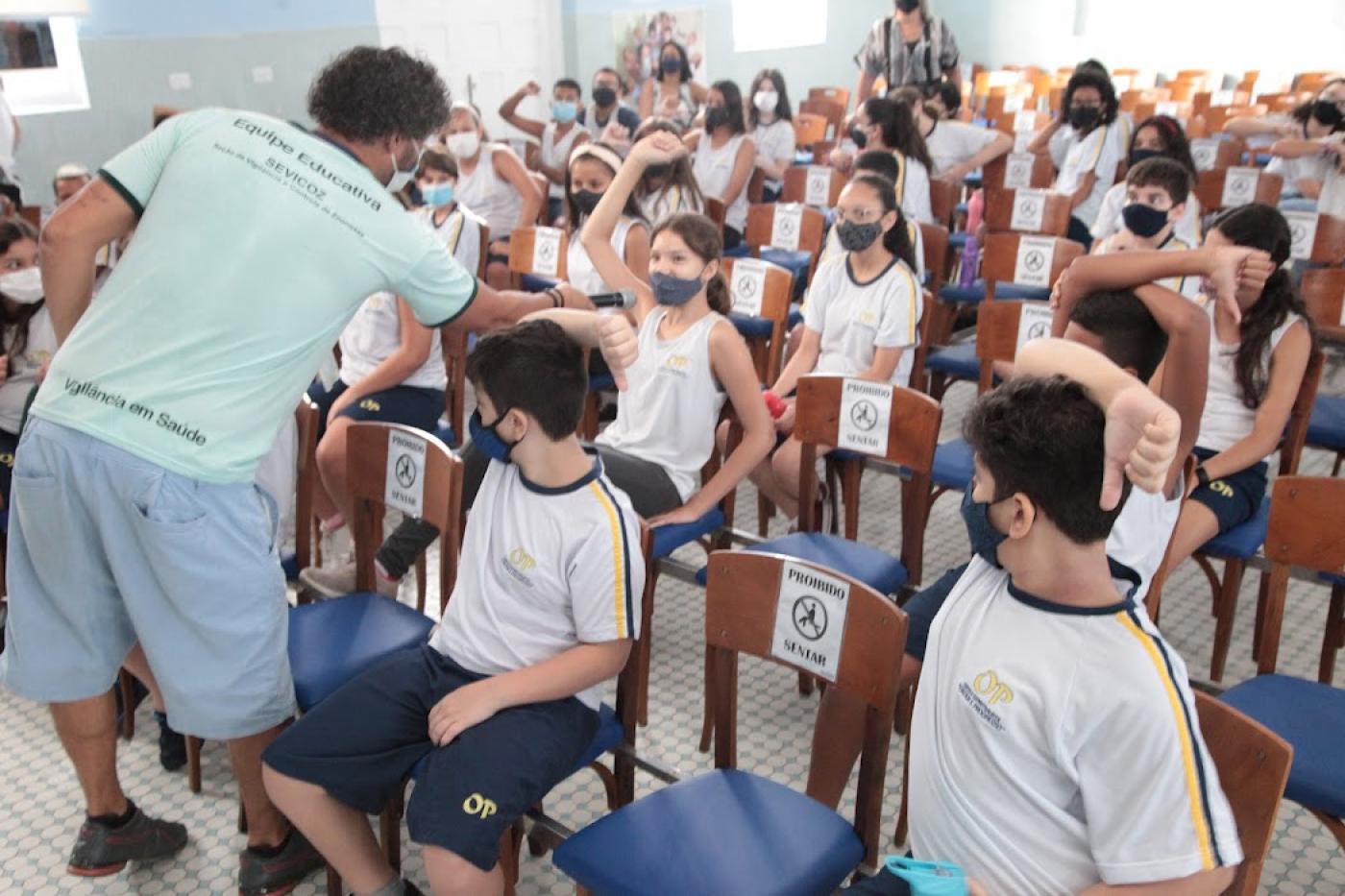 palestrante fala com criança em sala cheia de estudantes #paratodosverem