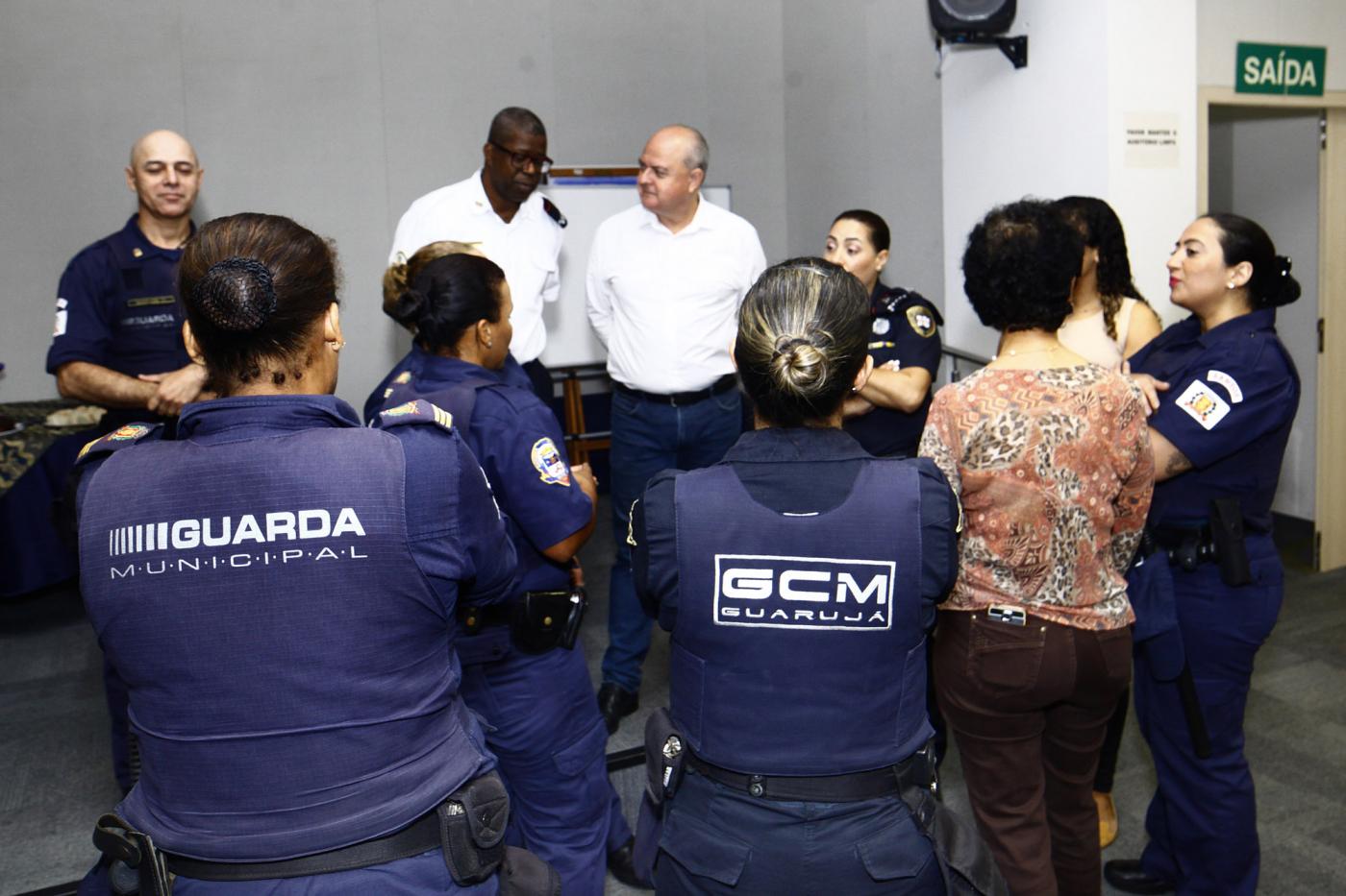 Guardam estão em pé, uniformizados e conversando em uma sala. #Pracegover