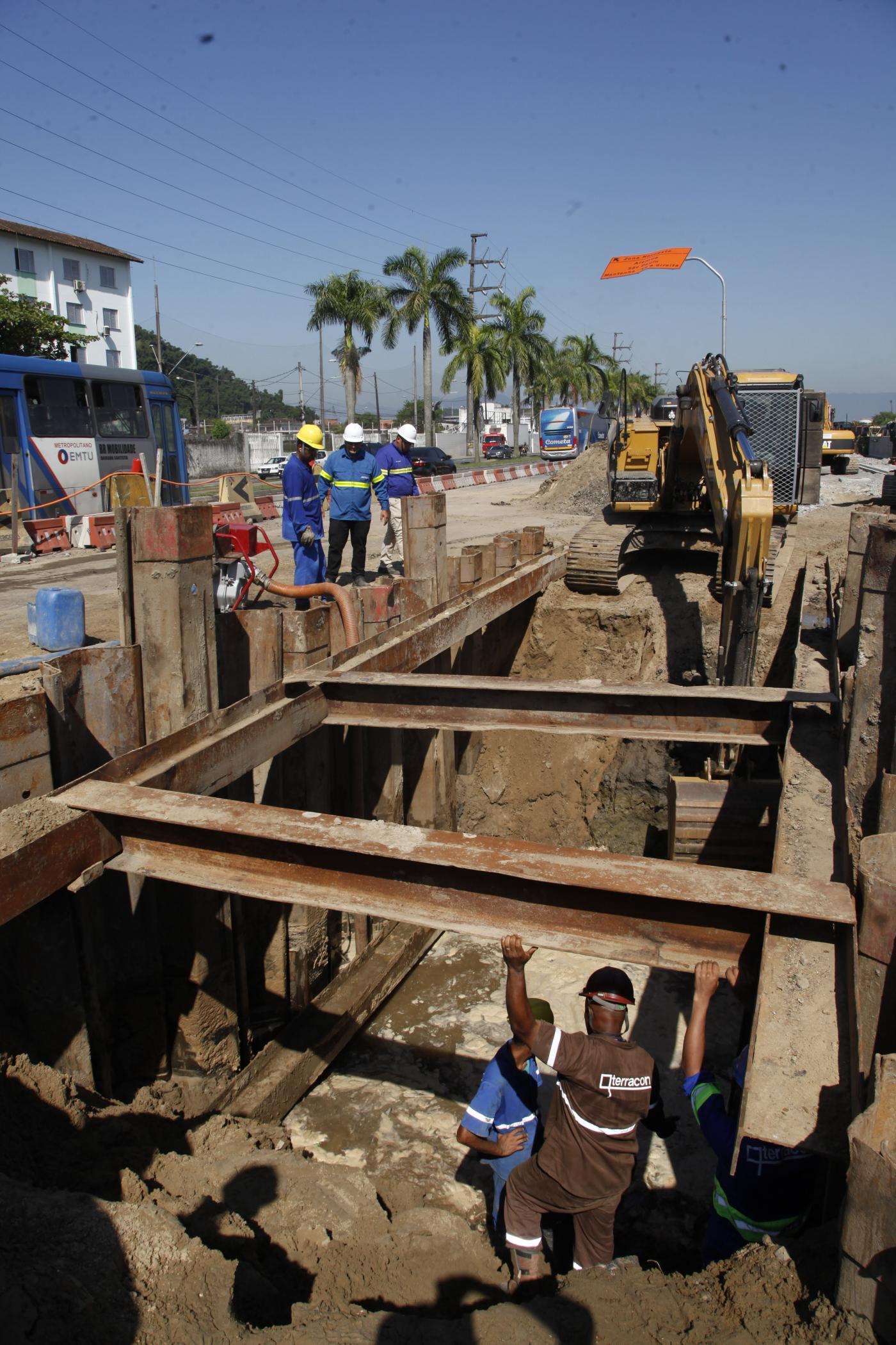 Subsolo é escavado para continuidade da ampliação de pontilhão. Homens e máquinas estão trabalhando. #Paratodosverem