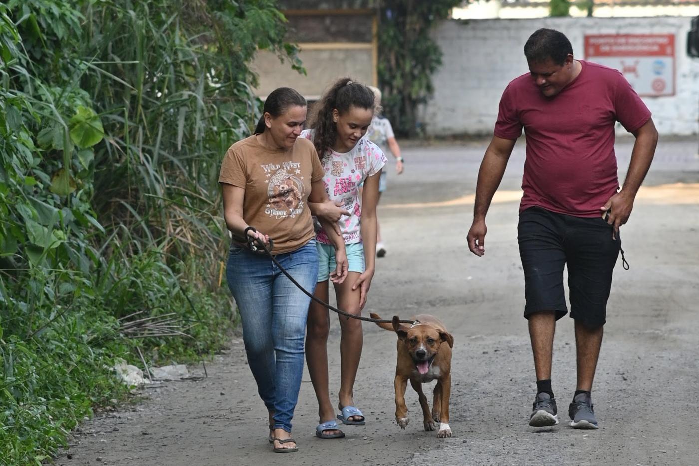 família de três pessoas caminha com cão. #paratodosverem
