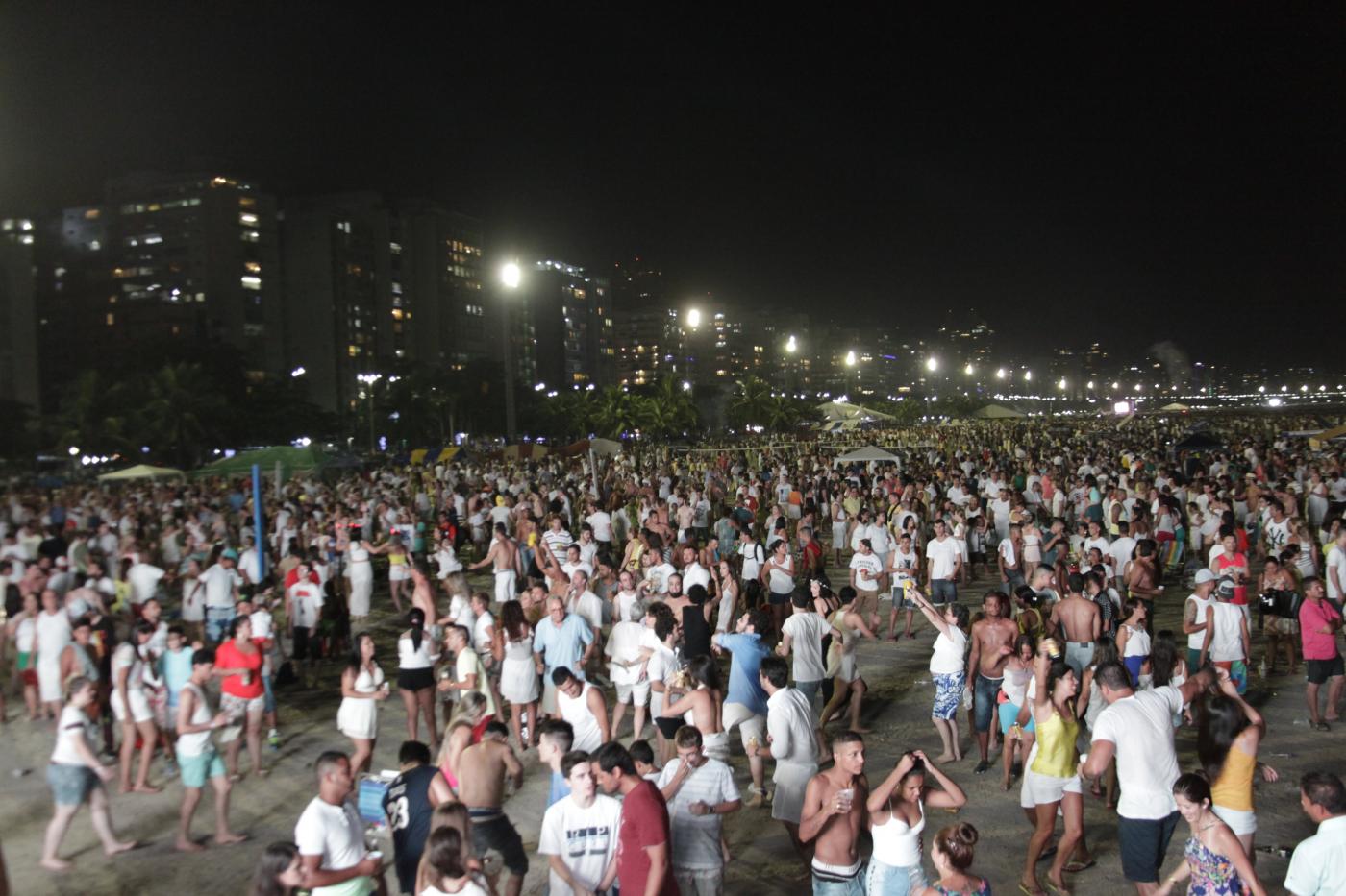 Praia lotada de pessoas à noite. #Pracegover