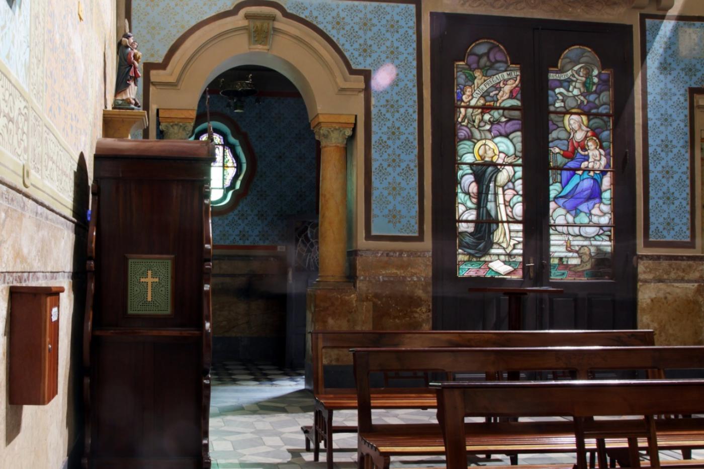 Interior da igreja do rosário, com bancos, paredes decoradas com azulejos e vitrais ao fundo. #paratodosverem