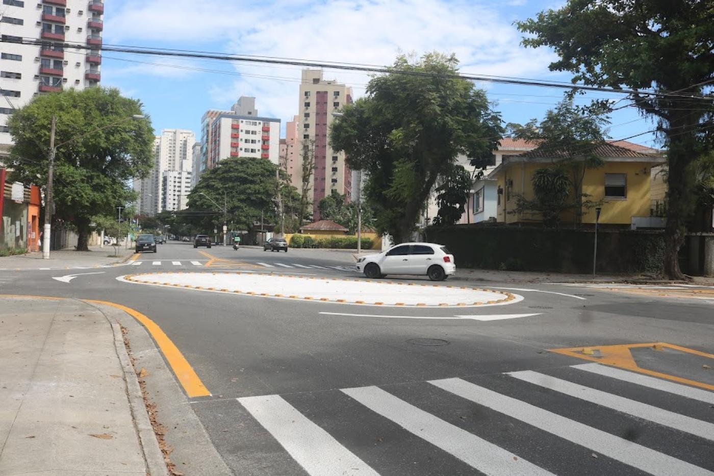 faixa de segurança em primeiro plano, calçada à esquerda e rotatória à frente com carro circulando. #paratodosverem