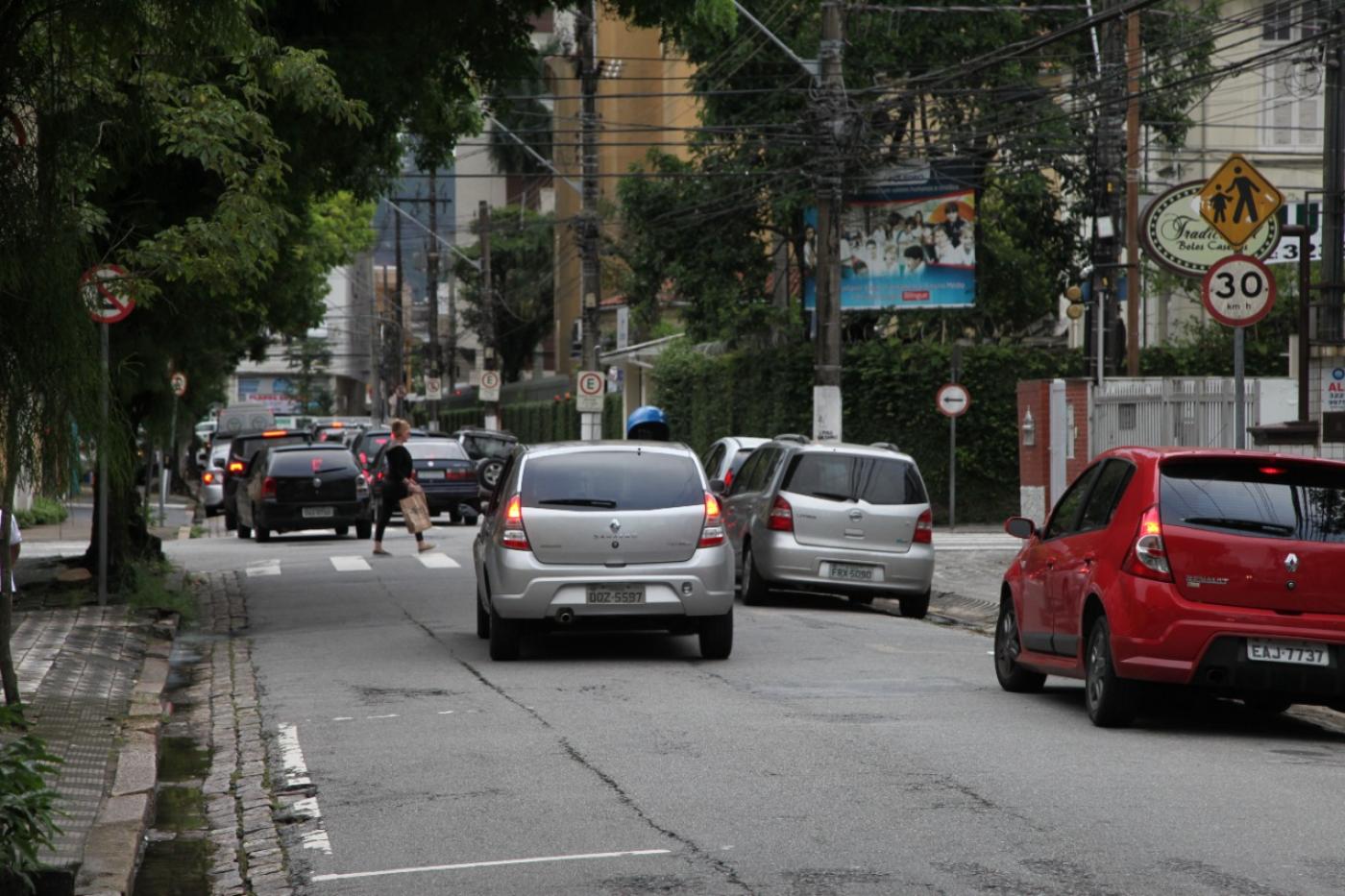 Rua com carros estacionado à direita e outros circulando. #paratodosverem