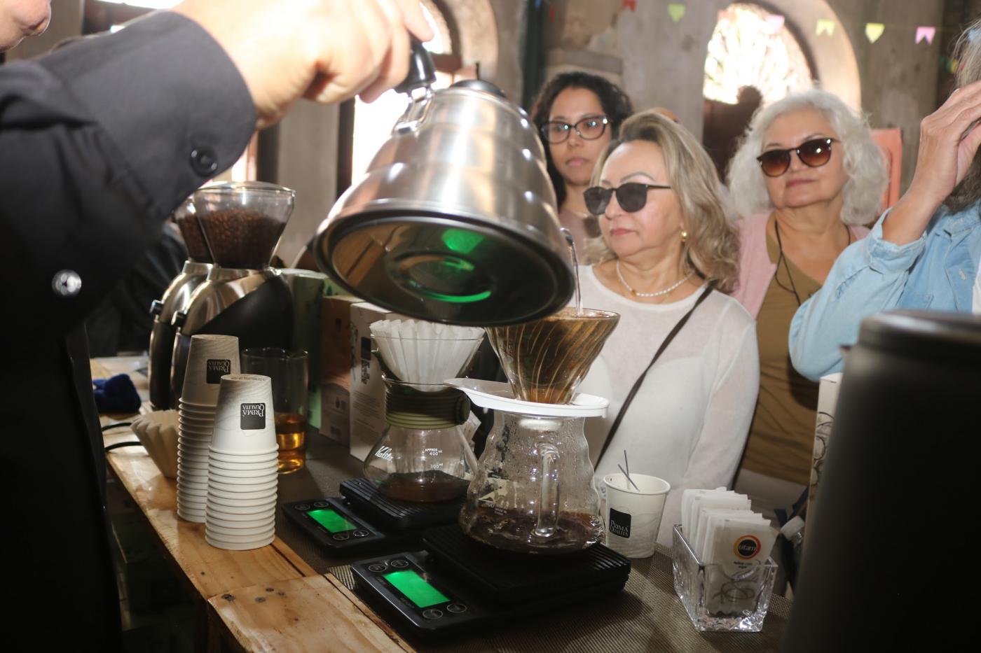 mão seguram bule e servem café para público. #paratodosverem