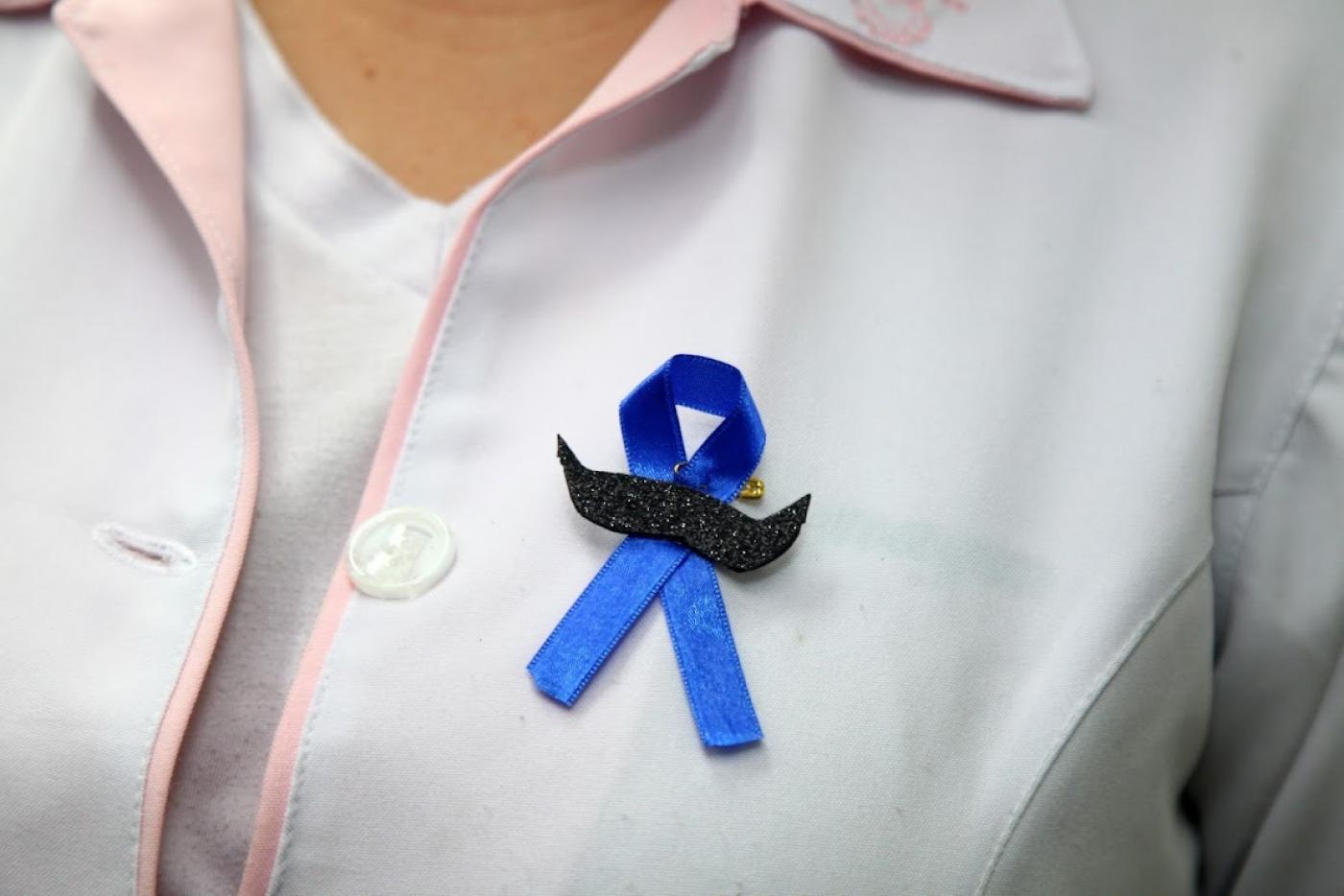 Simbolo do novembro azul no jaleco de uma profissional de saúde #paratodosverem