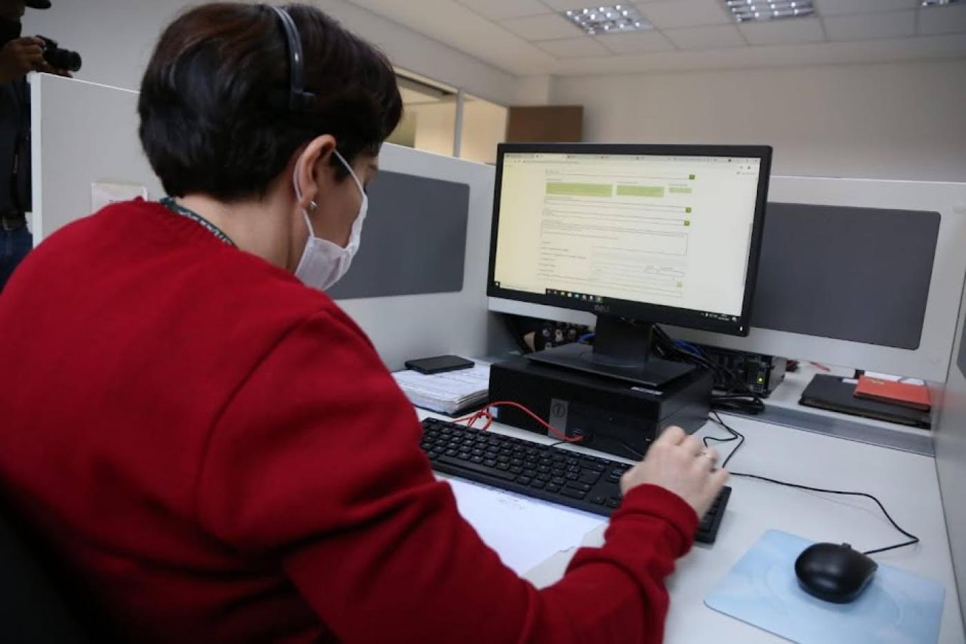 Mulher, com roupa vermelha, trabalha olhando para tela do computador. #pracegover