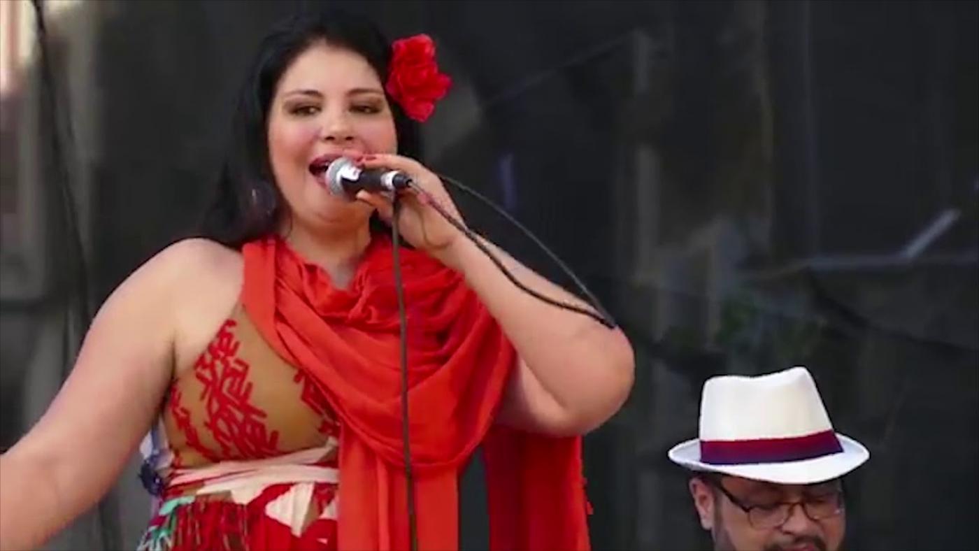 simone ancelmo está cantando. Ela segura um microfone. Tem uma flor vermelha na cabeça. #paratodosverem 