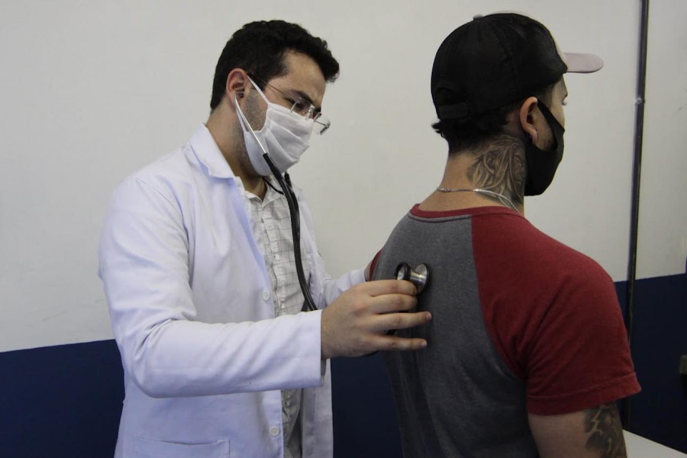 médico segura estetoscópio nas costas de paciente para fazer ausculta. #paratodosverem