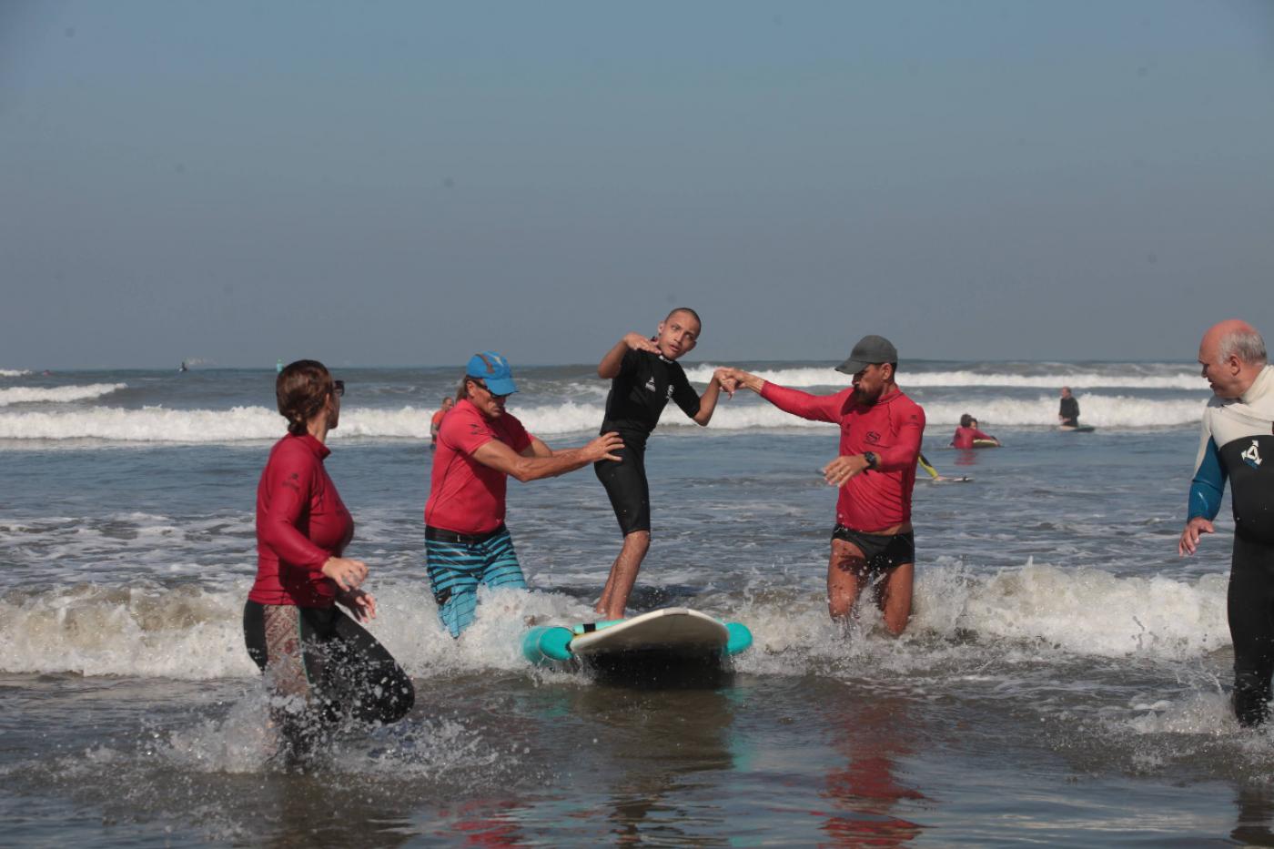 Jovem com deficiência pratica surfe adaptado com ajuda de instrutores. #paratodosverem
