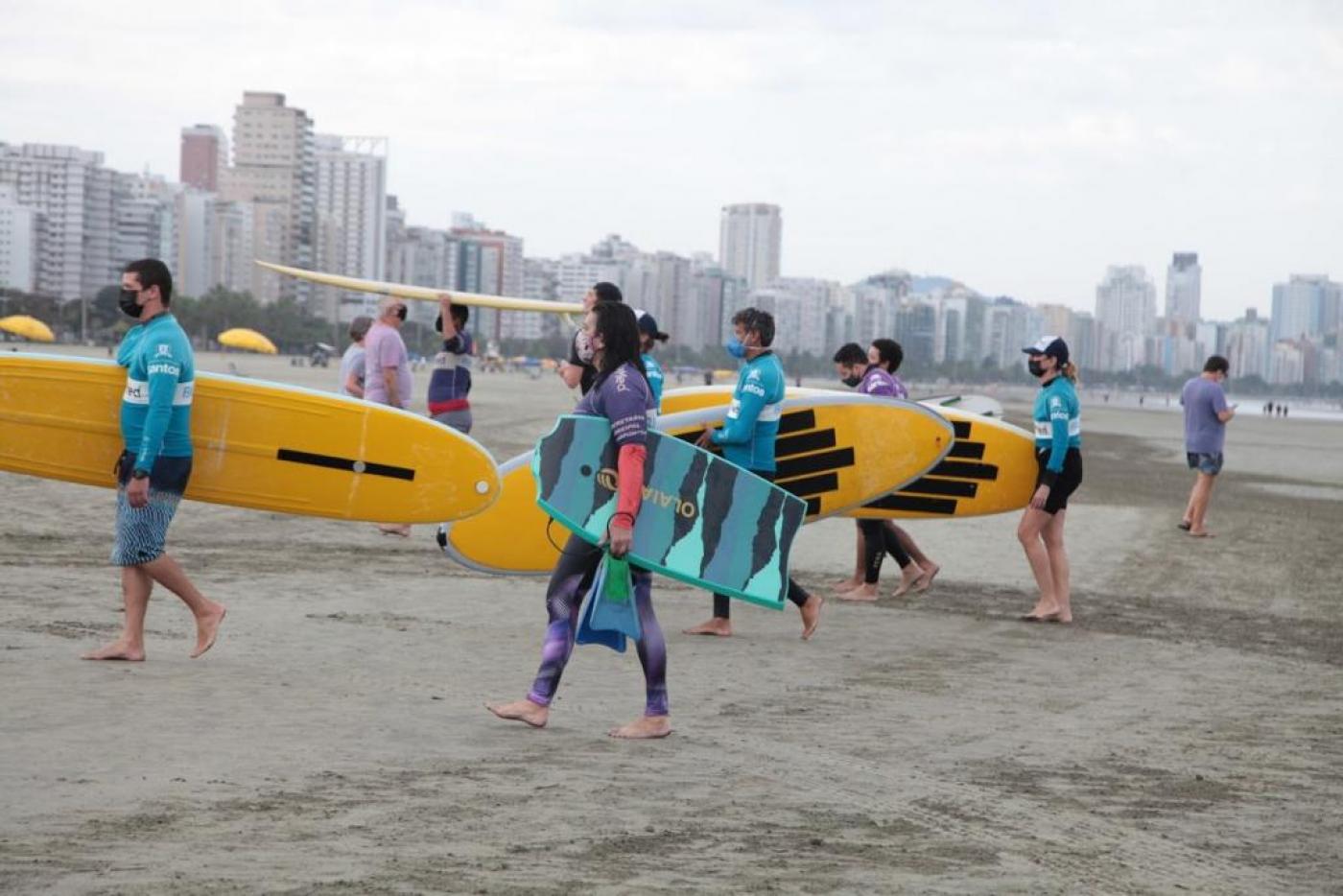 Surfistas seguram a prancha na areia da praia. #paratodosverem